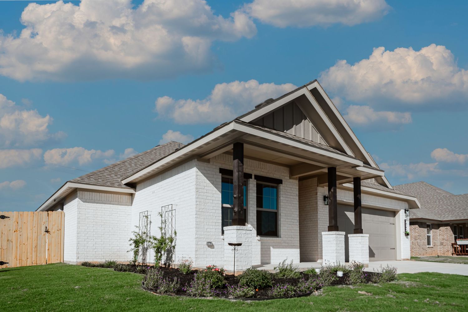 White residential homes with porches line a suburban street under puffy white clouds in a blue sky.
