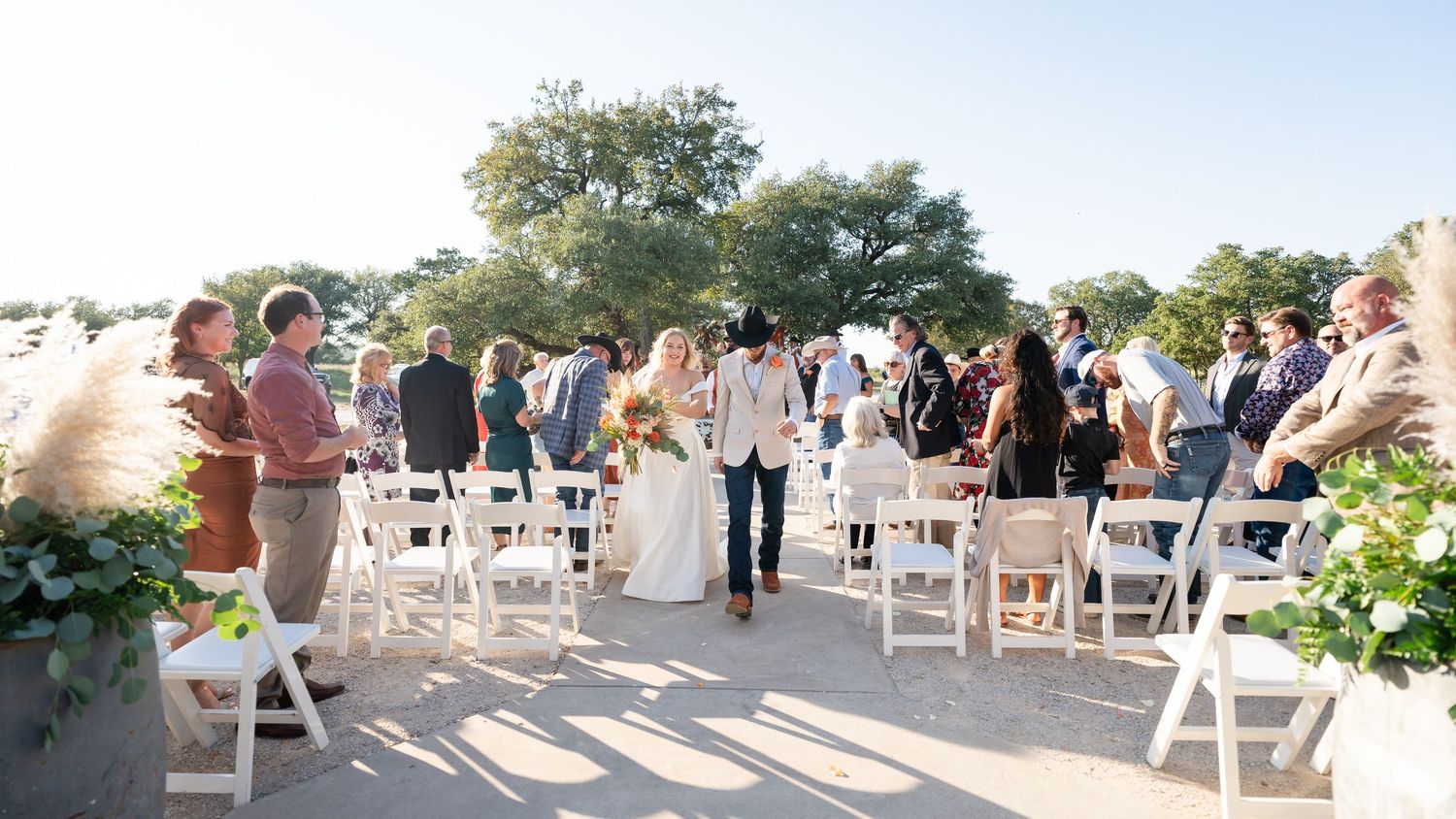 Outdoor wedding ceremony setup with white chairs arranged in rows under trees.