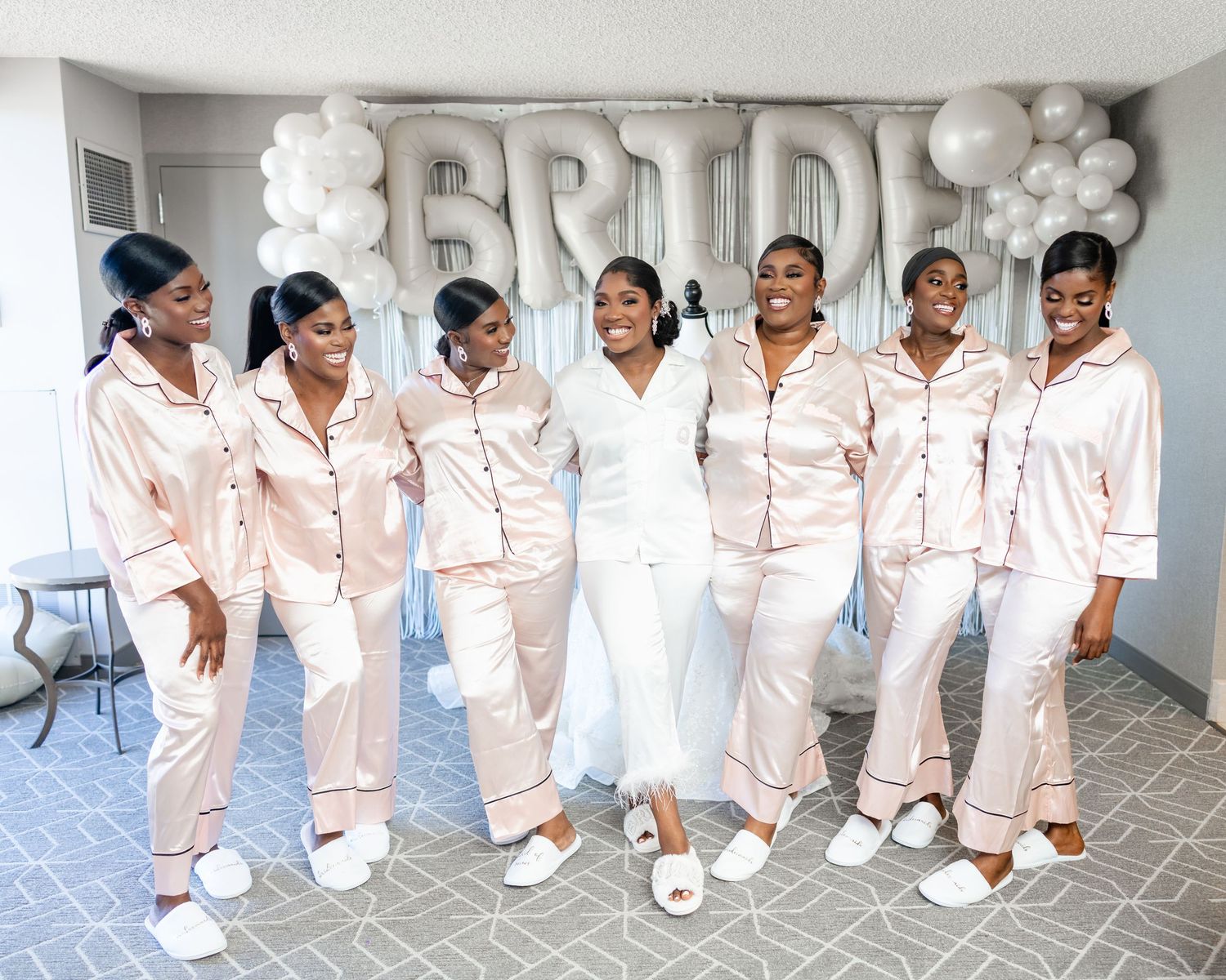 Bridal party in matching white satin pajamas sitting together on floor.