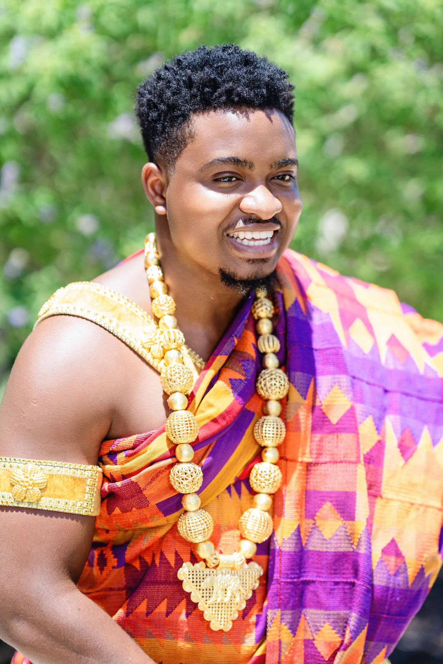 Traditional African wedding attire featuring vibrant orange and purple fabric with gold accents and jewelry.