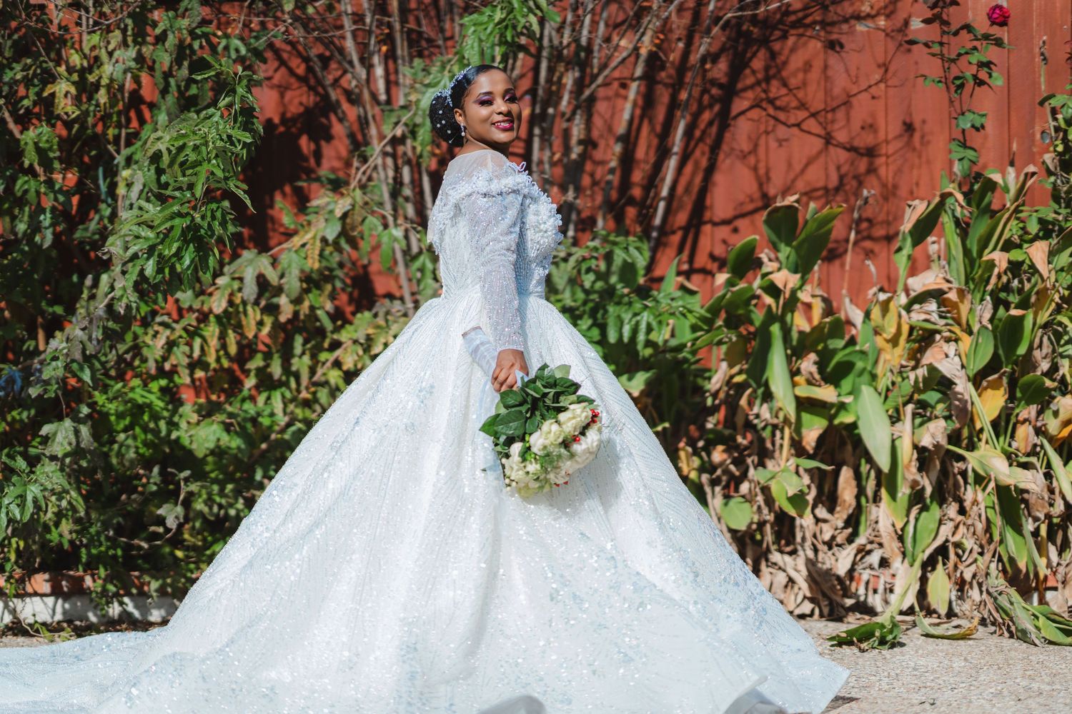 Stunning bride in white ballgown holds bouquet against red wall backdrop.