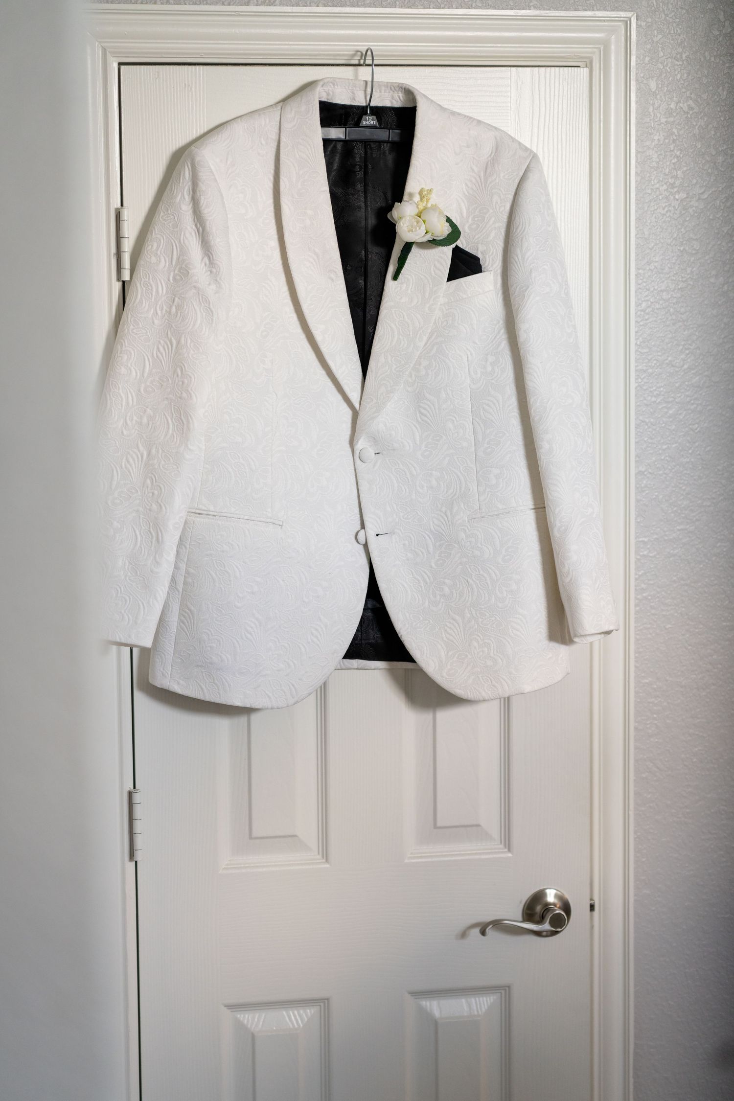 White formal blazer jacket hanging on a white door displaying elegant wedding attire.