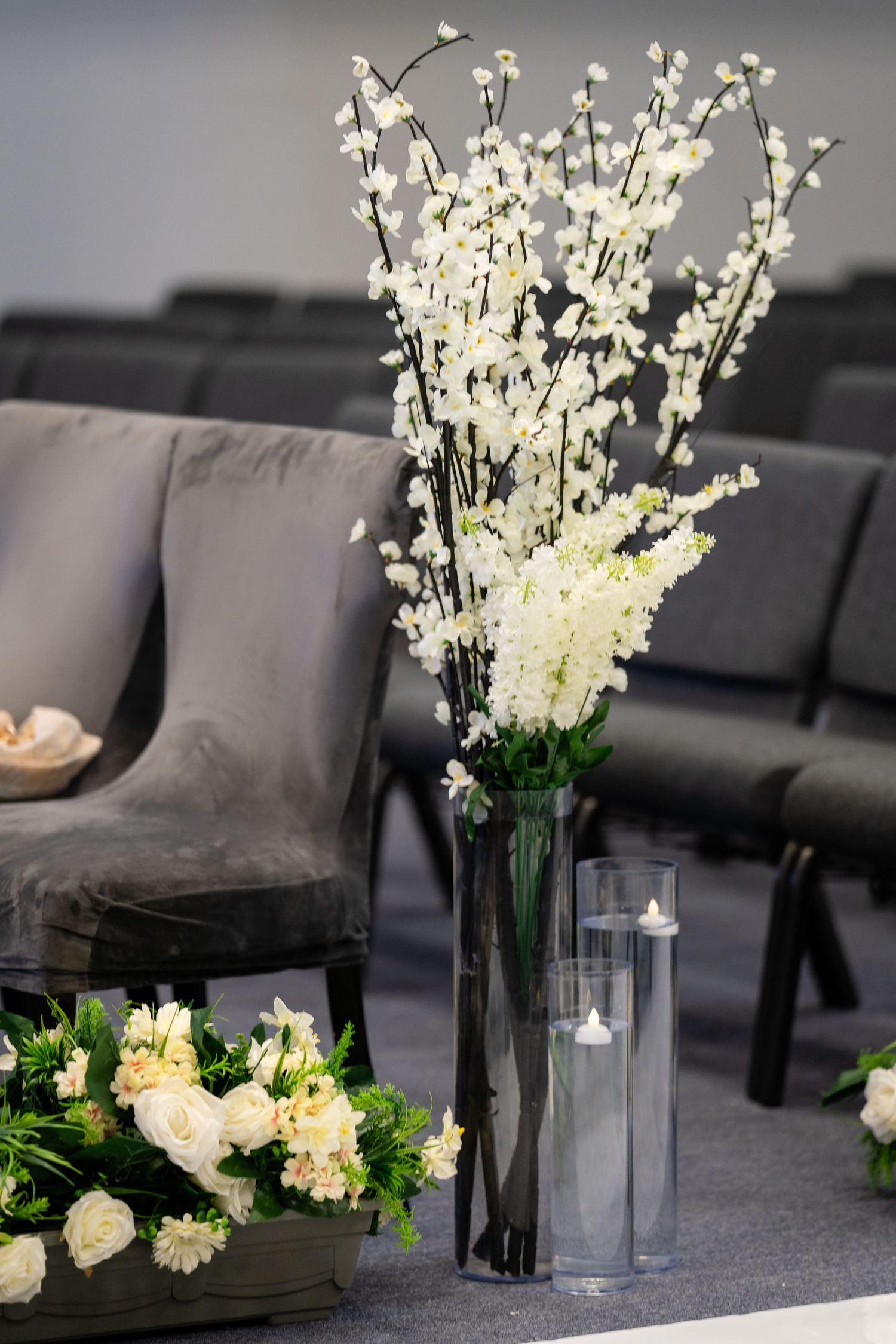 Modern wedding ceremony setup with white cherry blossoms and glass vases against grey seating.