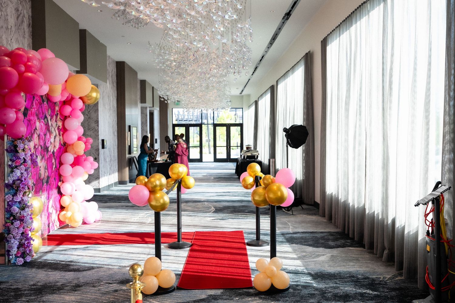 A long hallway decorated with colorful balloons and a red carpet runner creates a festive atmosphere.