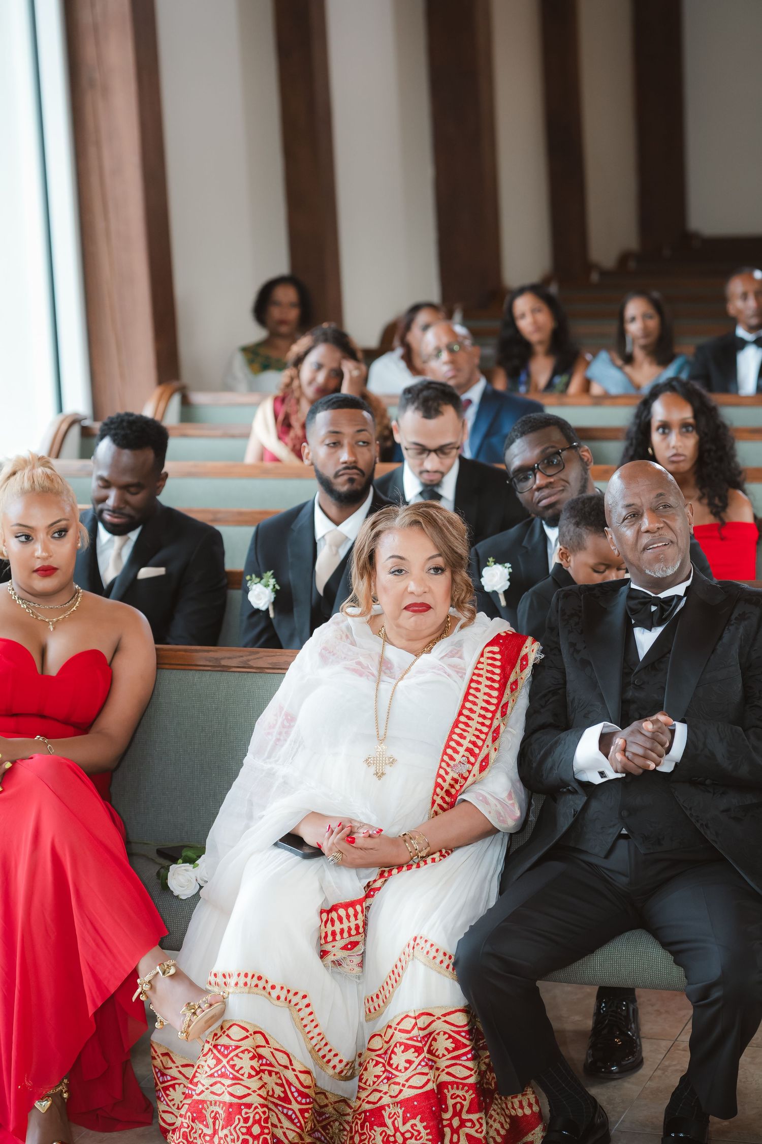 Wedding guests seated in church pews wearing formal attire in red and black color scheme.