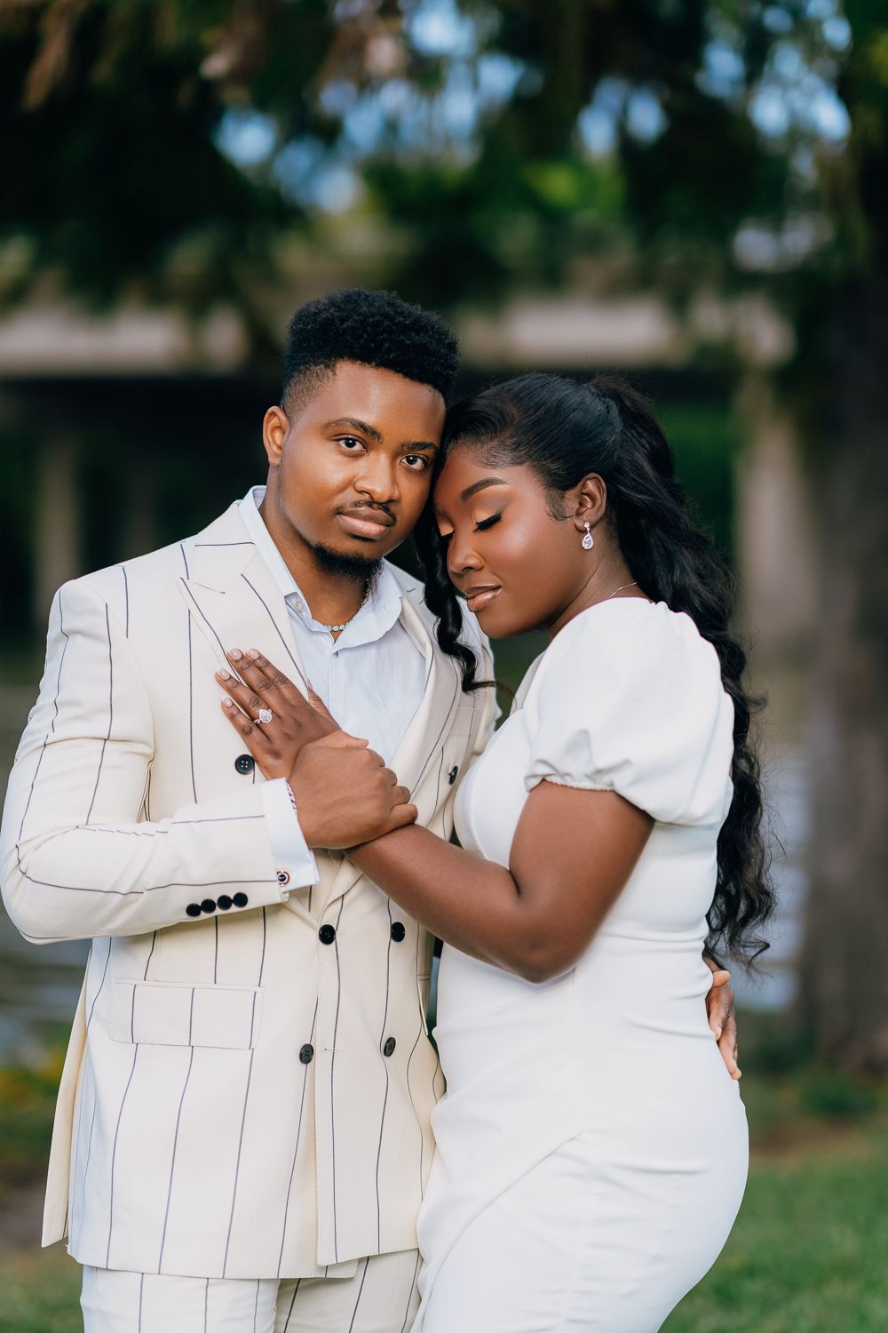 A romantic couple in white outfits share tender moments together in a series of outdoor engagement photos.