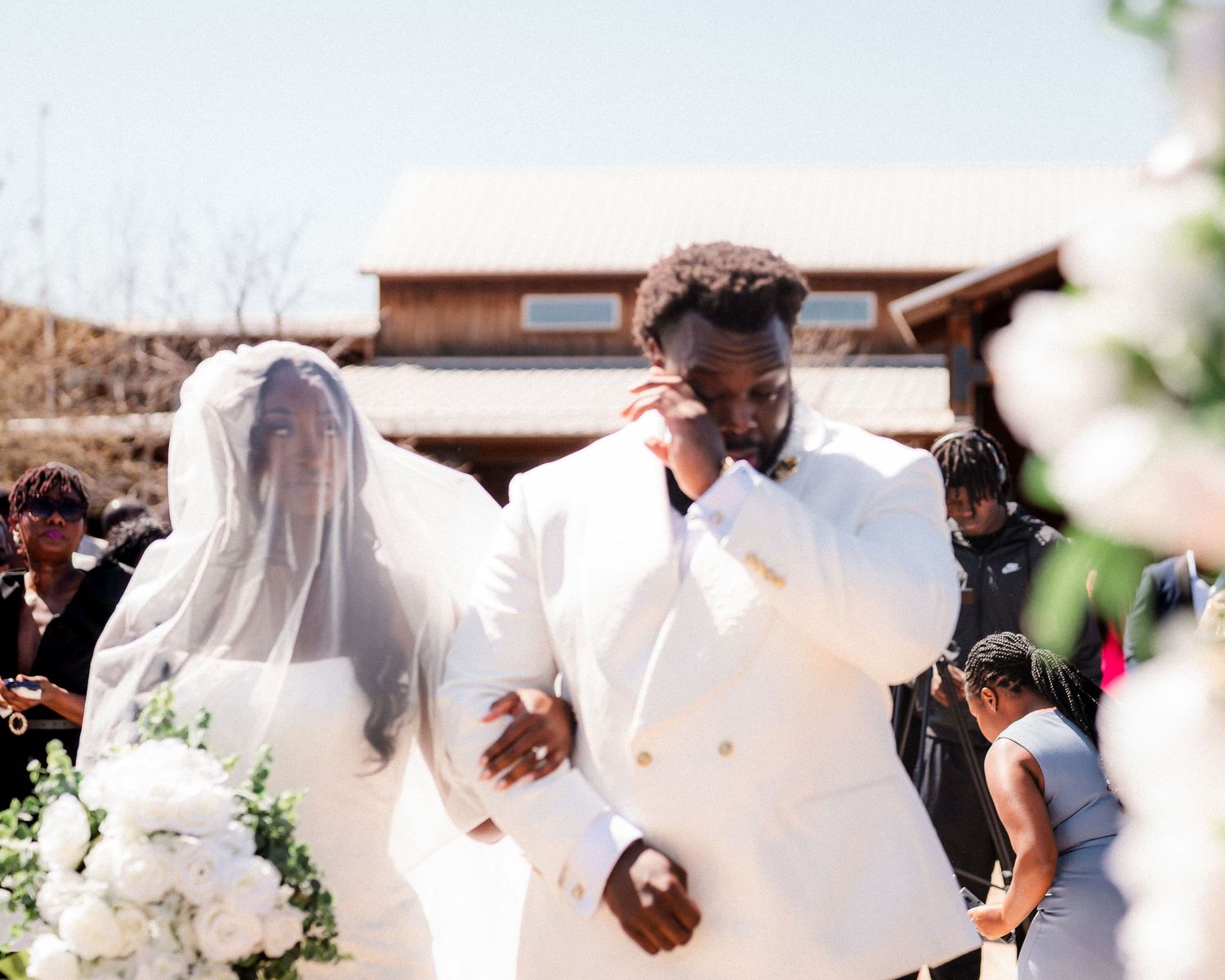 A wedding celebration scene with a couple dancing outdoors surrounded by guests and white decor.