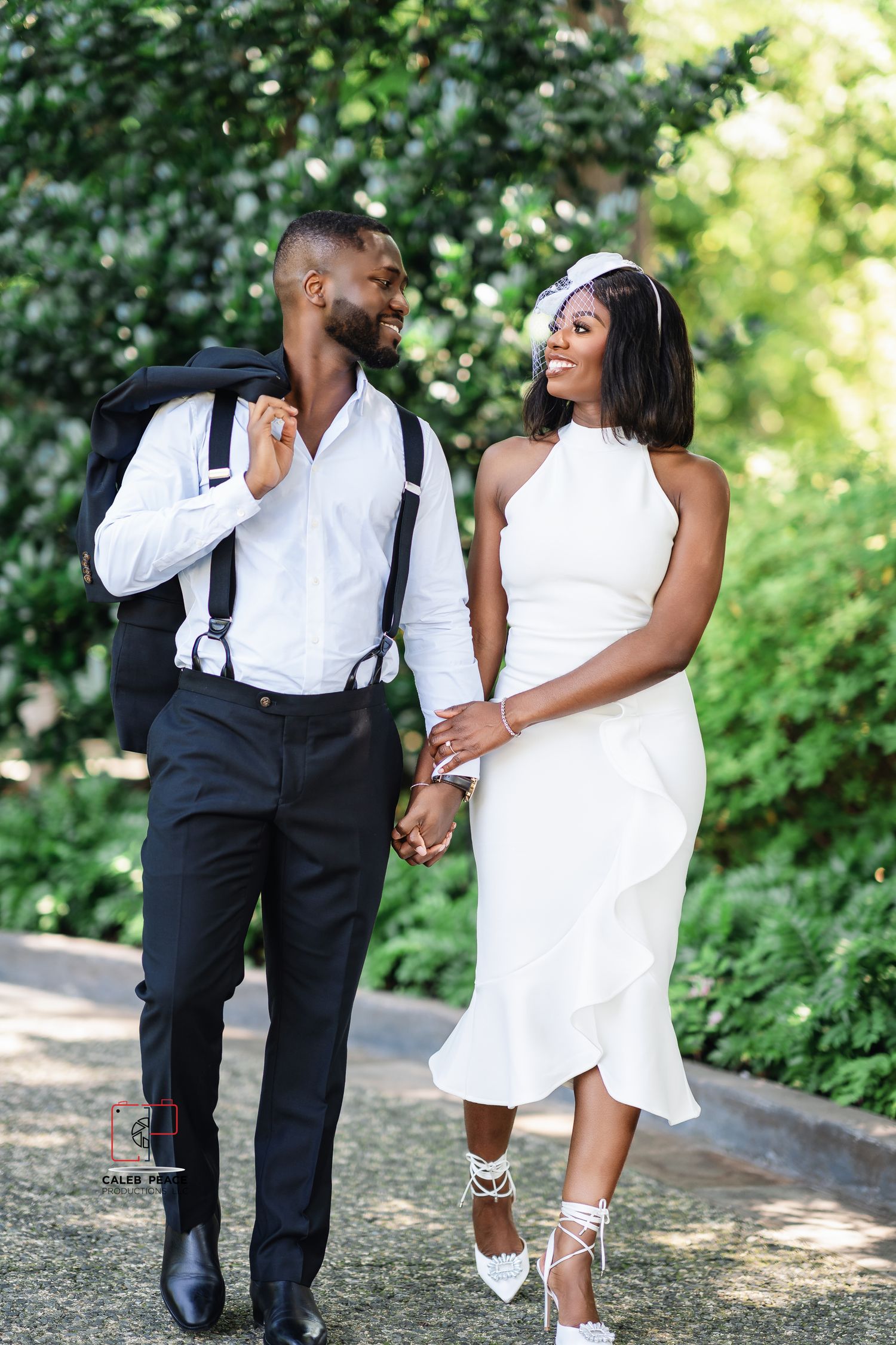 Elegant couple walking together outdoors, wearing coordinated white and black formal attire in a garden setting.