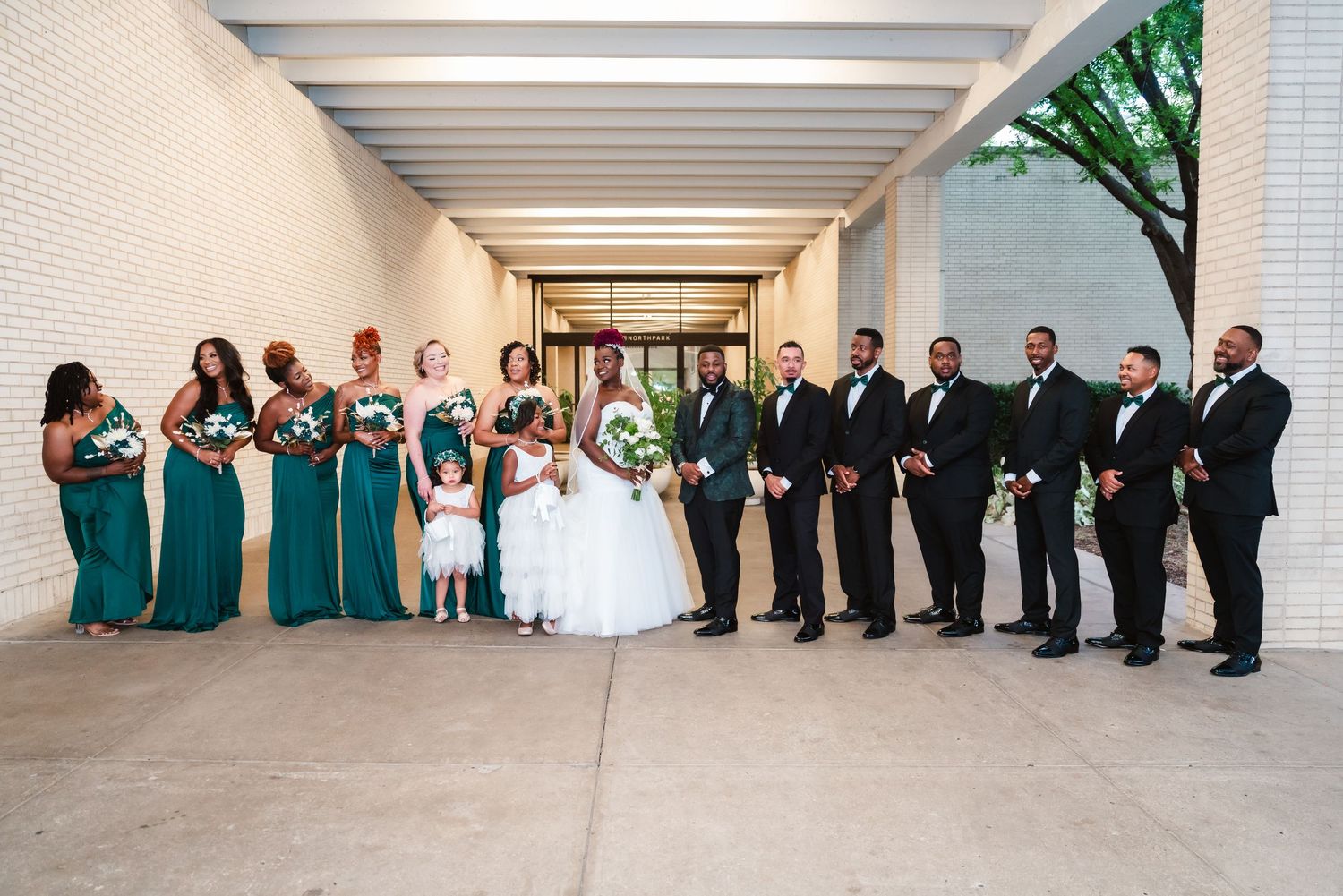 Wedding party members lined up against white wall in coordinated teal and black attire.