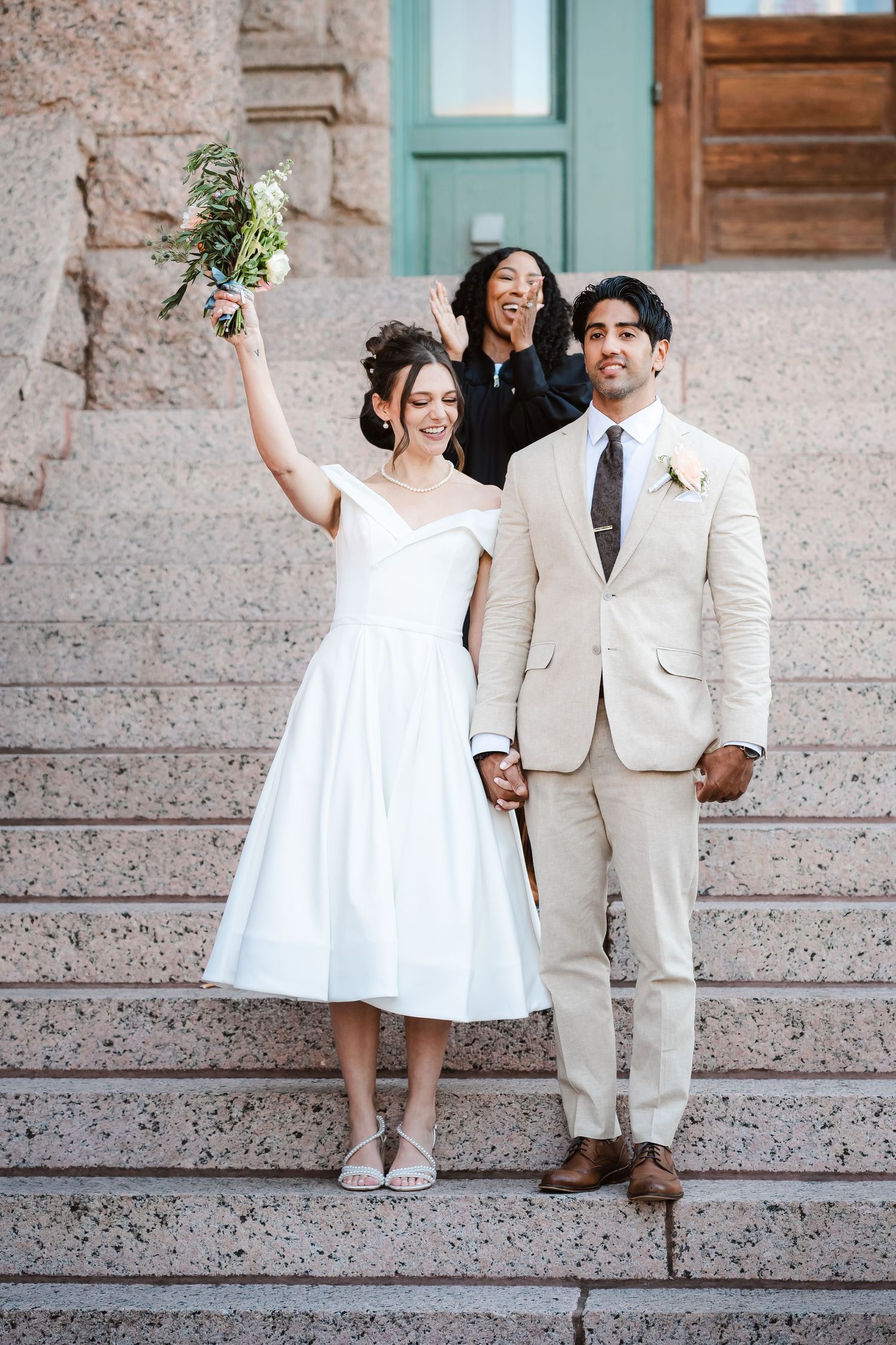 A joyful wedding celebration moment on stone steps with a bride holding her bouquet high in celebration.