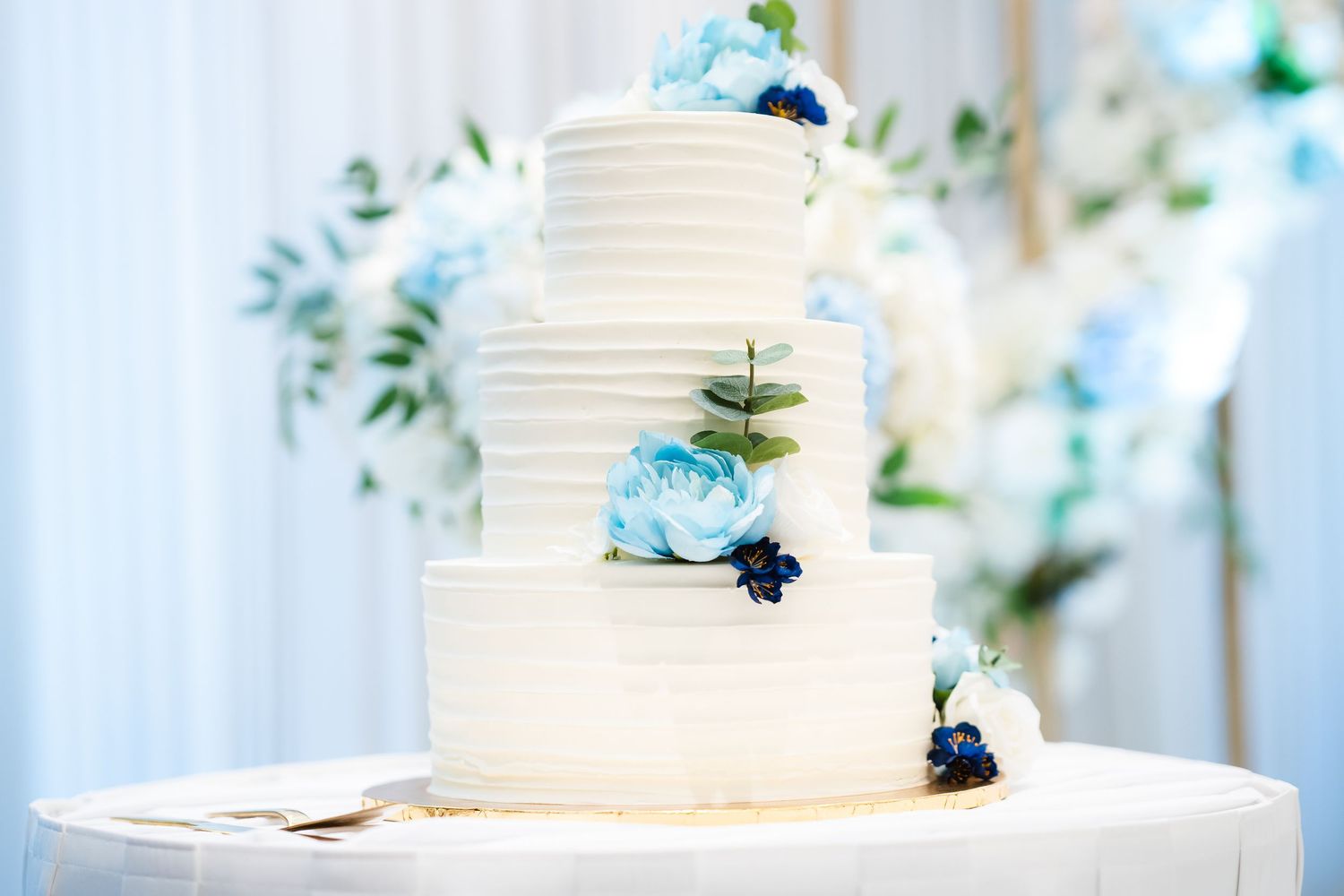 White wedding cake with fresh flowers displayed on a stand at an elegant reception venue with hanging lanterns.