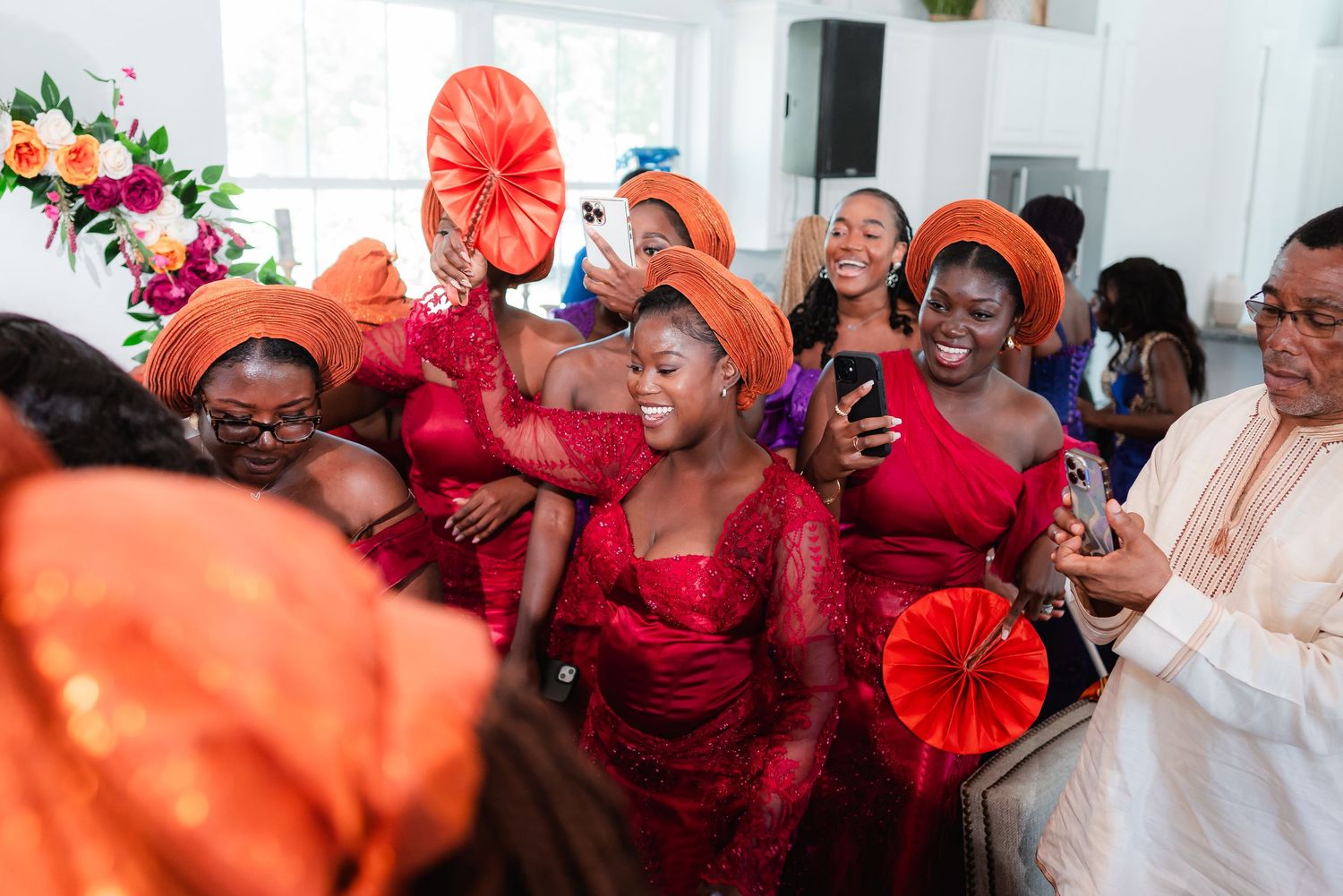 A joyous celebration with people wearing bright red and orange outfits and decorative fans.