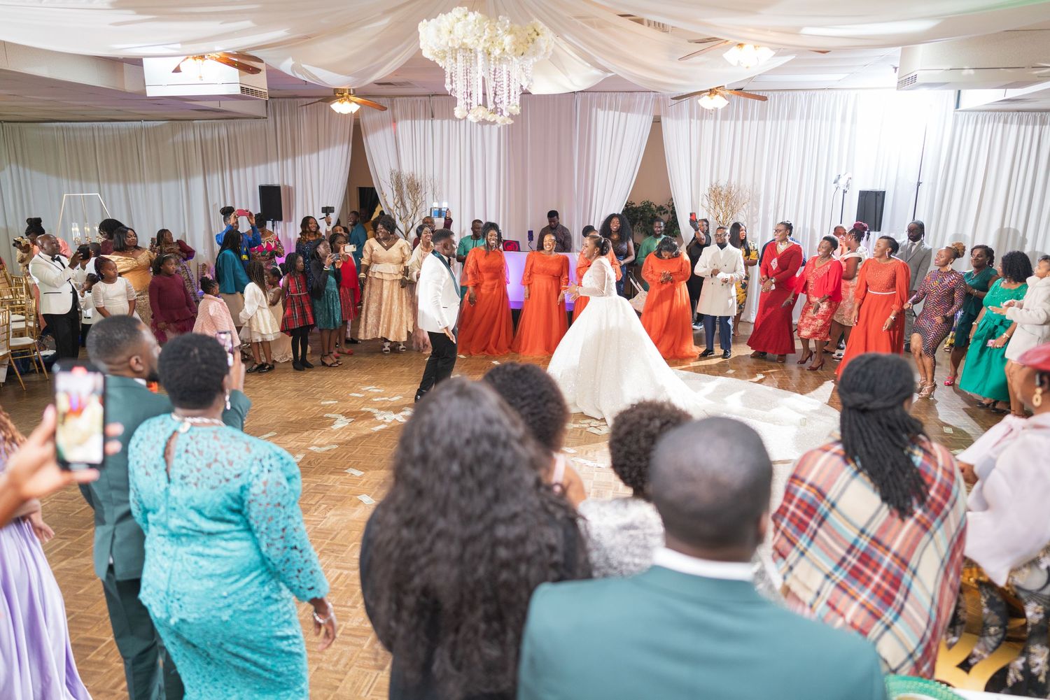 Wedding reception dance floor filled with celebrating guests in colorful attire under draped fabric ceiling.