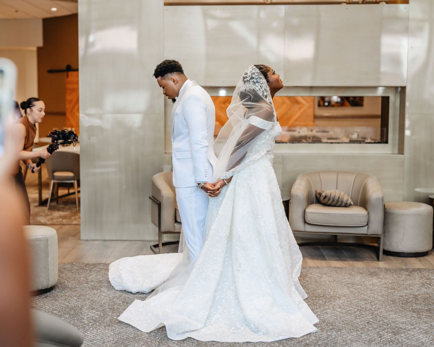 A bride in a flowing white gown sits gracefully on a plush gray carpet in an elegant indoor setting.