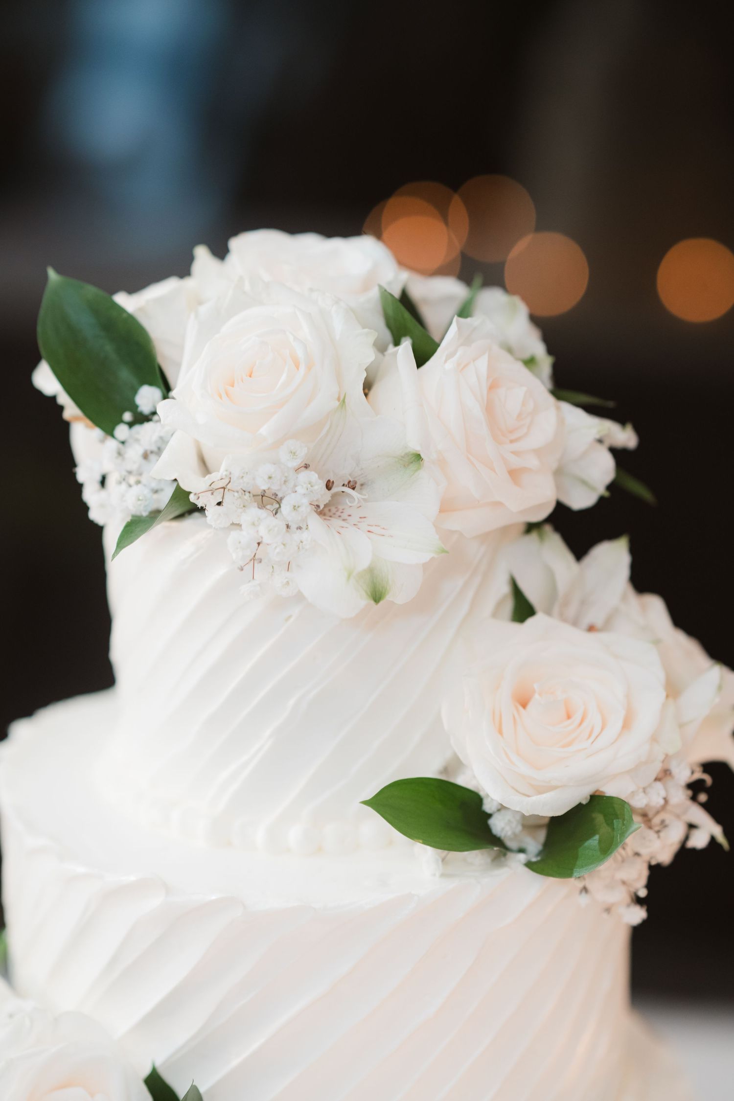 Elegant white wedding cake decorated with fresh roses and greenery.