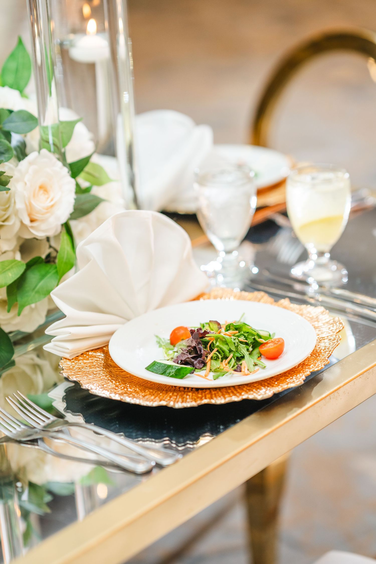 Close-up of wedding table settings with copper charger plates, white roses, and plated salads.