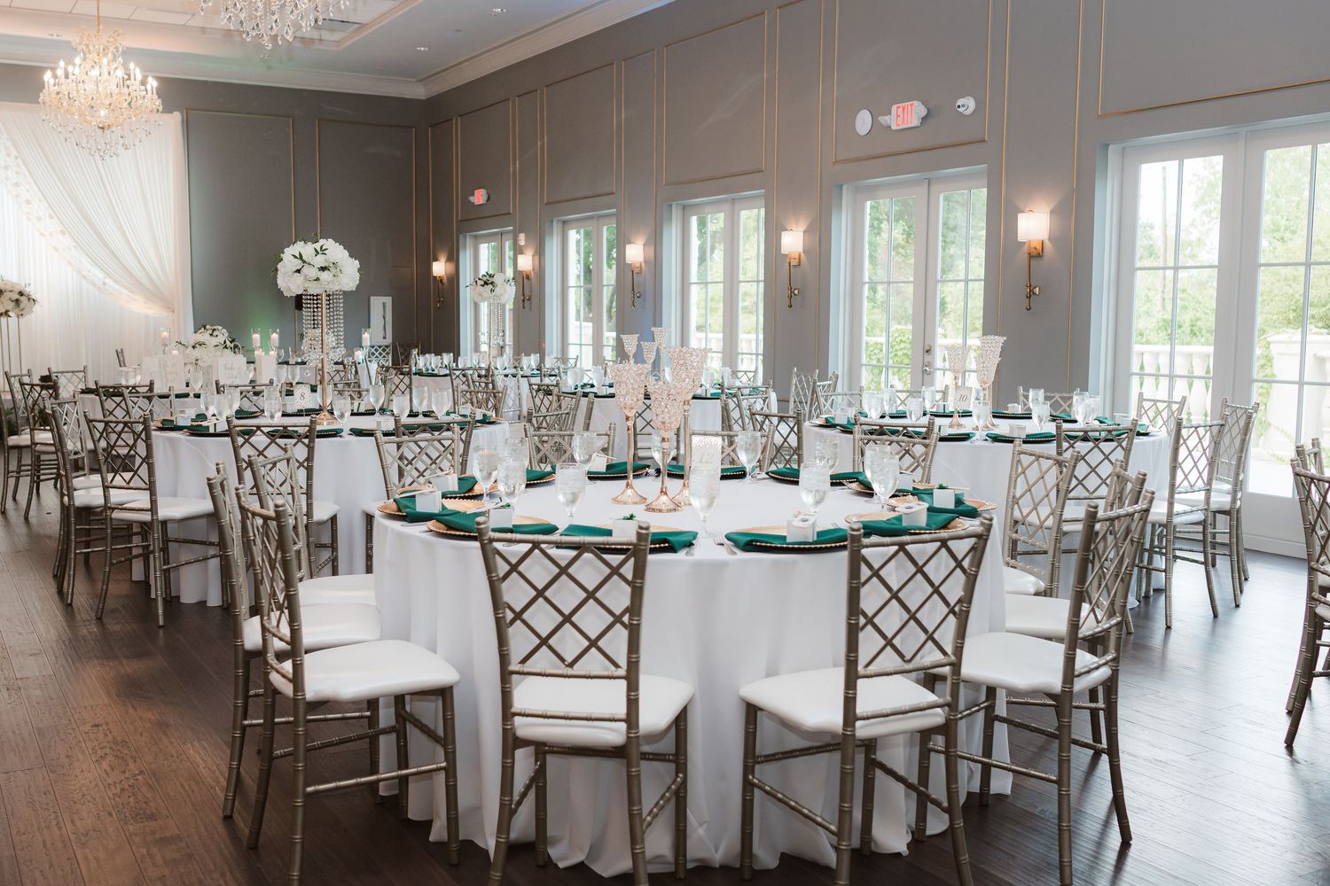 An elegant wedding reception venue with crystal chandeliers and white table settings arranged in a bright, airy ballroom.