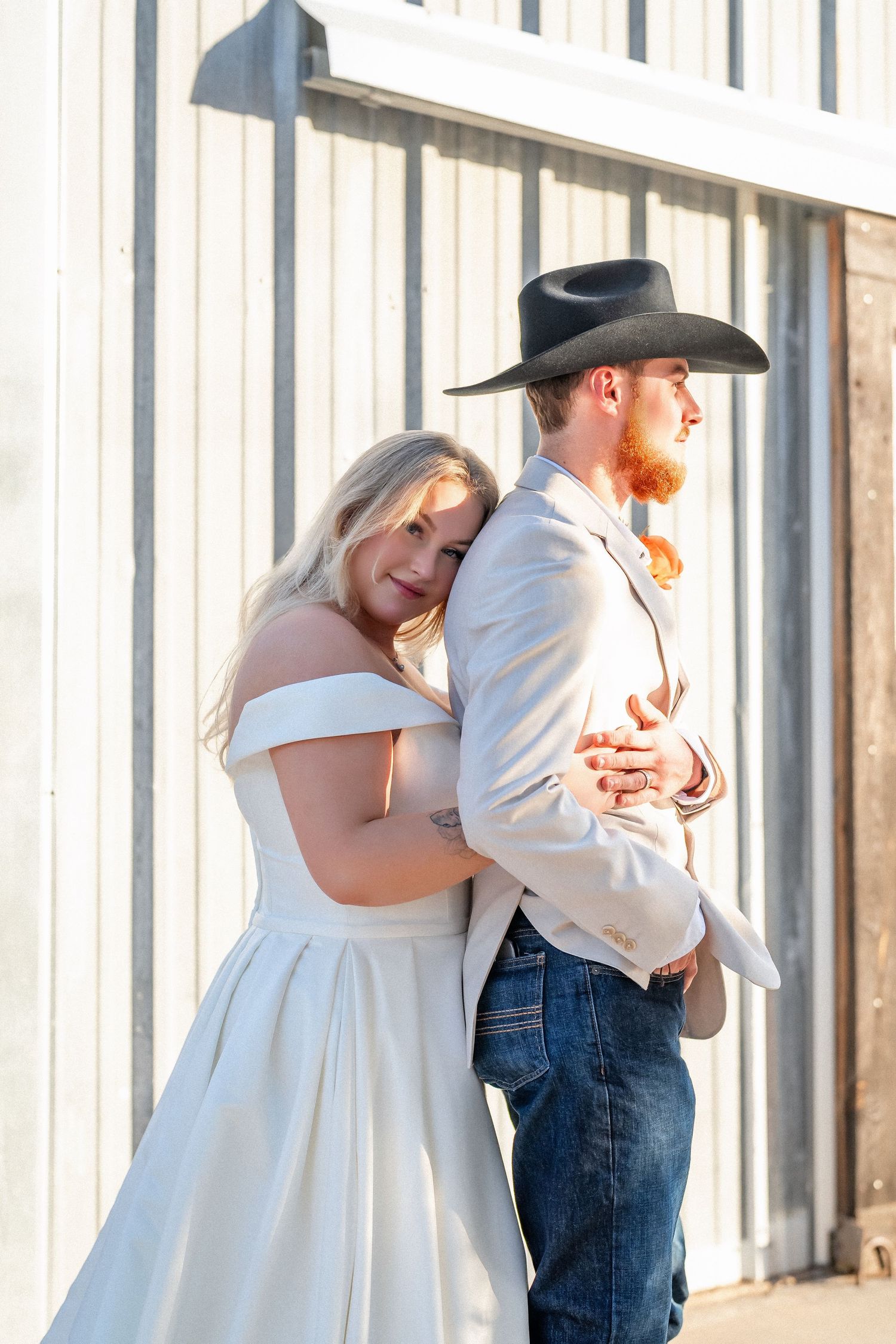 A couple in western attire shares a romantic dance, with the bride in white and groom in cowboy hat and jeans.