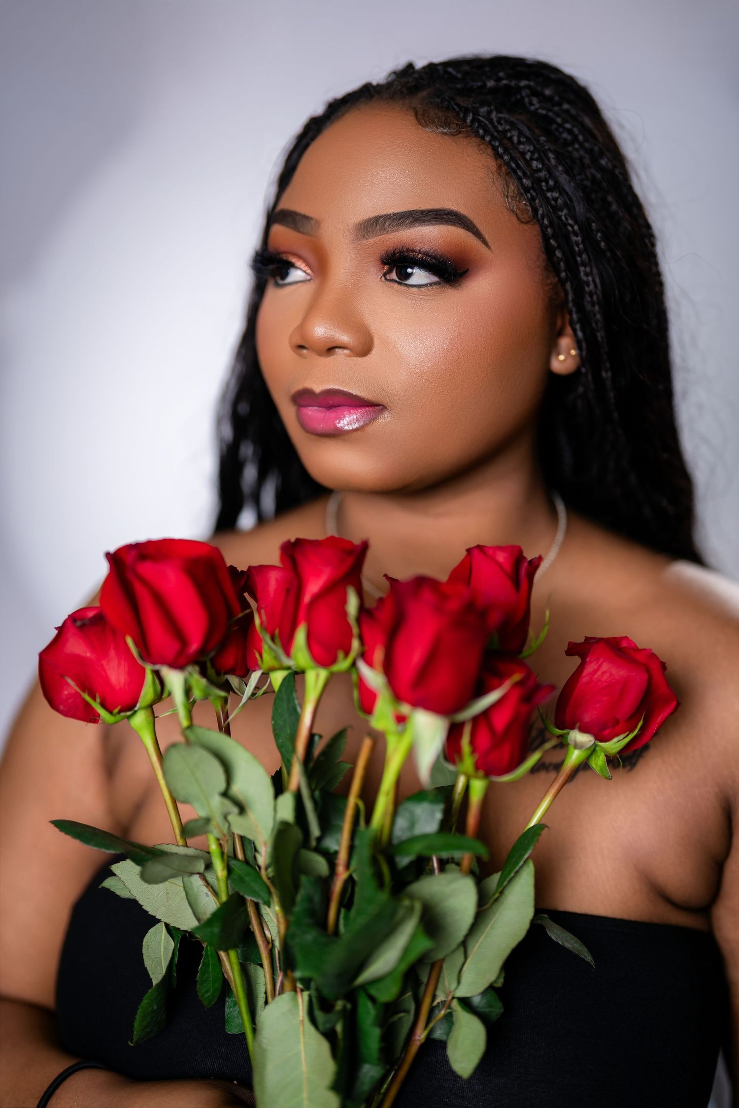 Glamorous portrait photoshoot featuring red roses against a dark background with dramatic lighting and makeup.