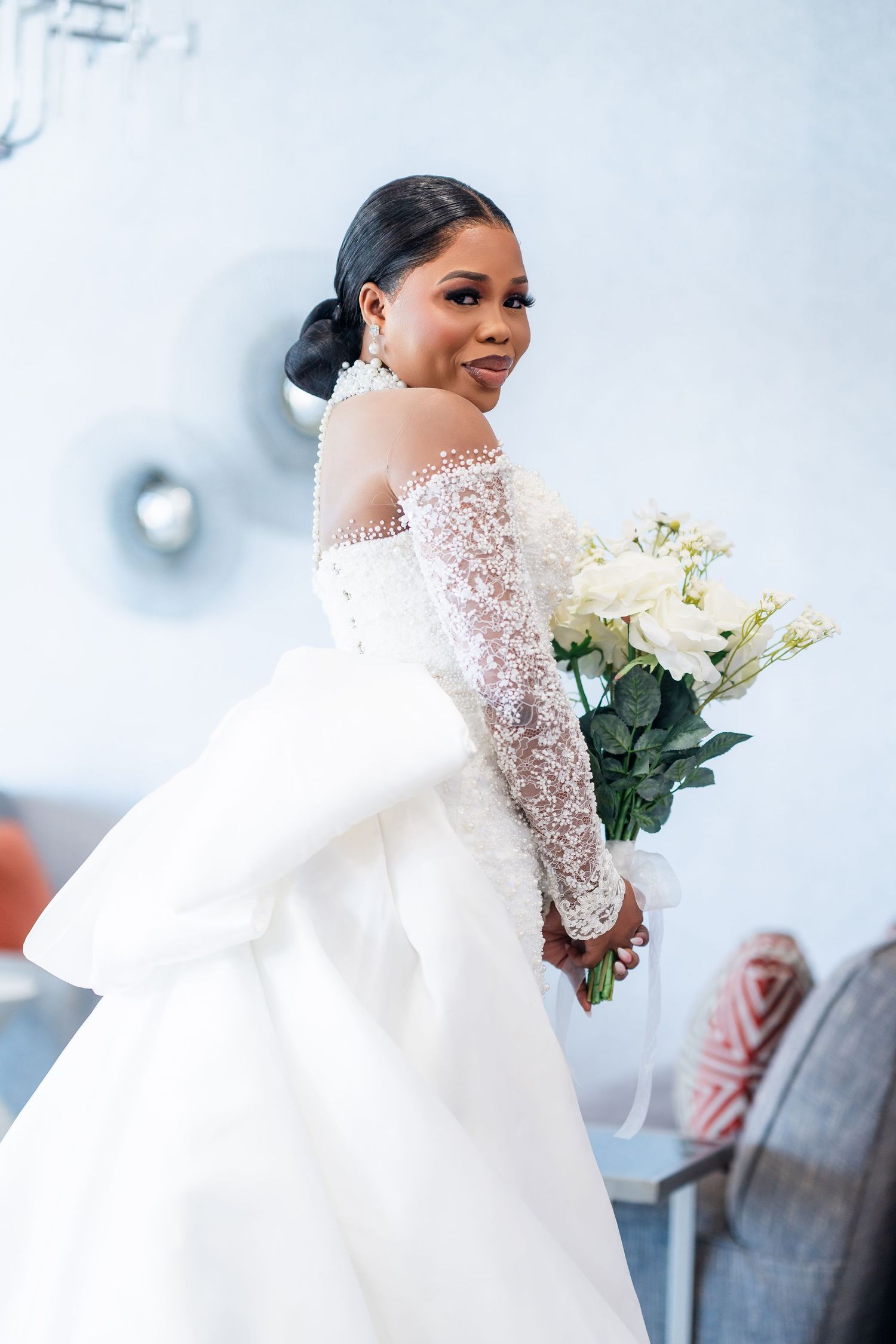 Elegant bride in a white lace gown with long sleeves holding a bouquet of white roses.