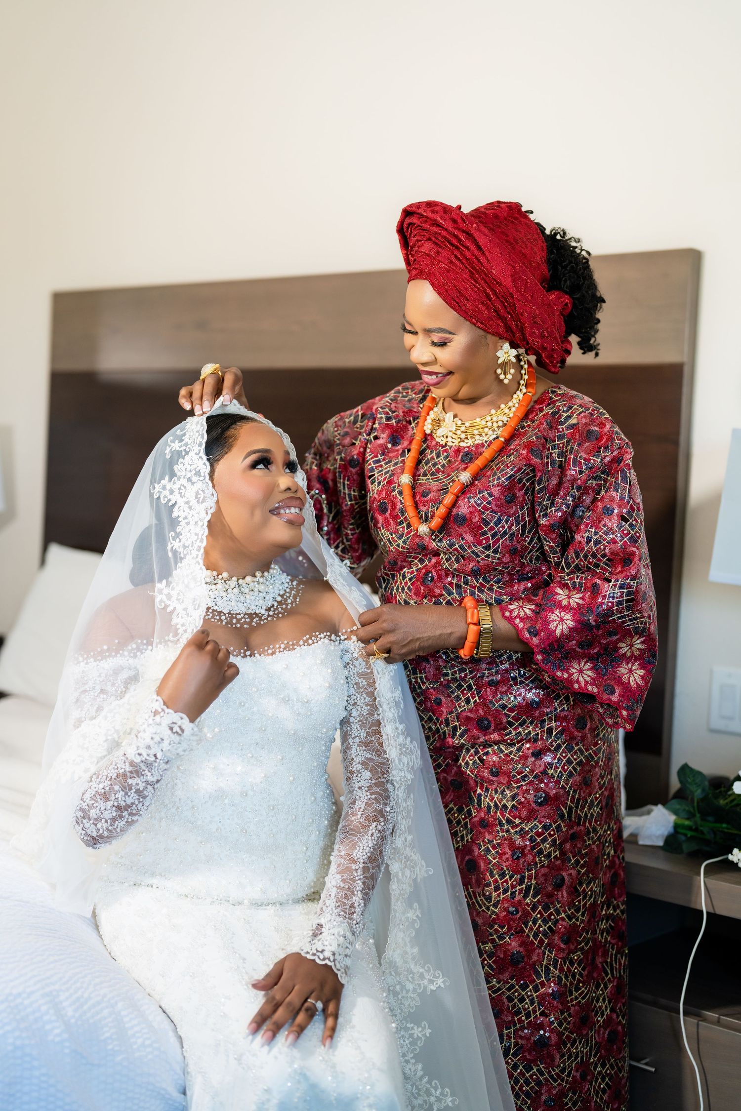 Bride in white lace gown shares celebratory moments with guests in traditional African attire.