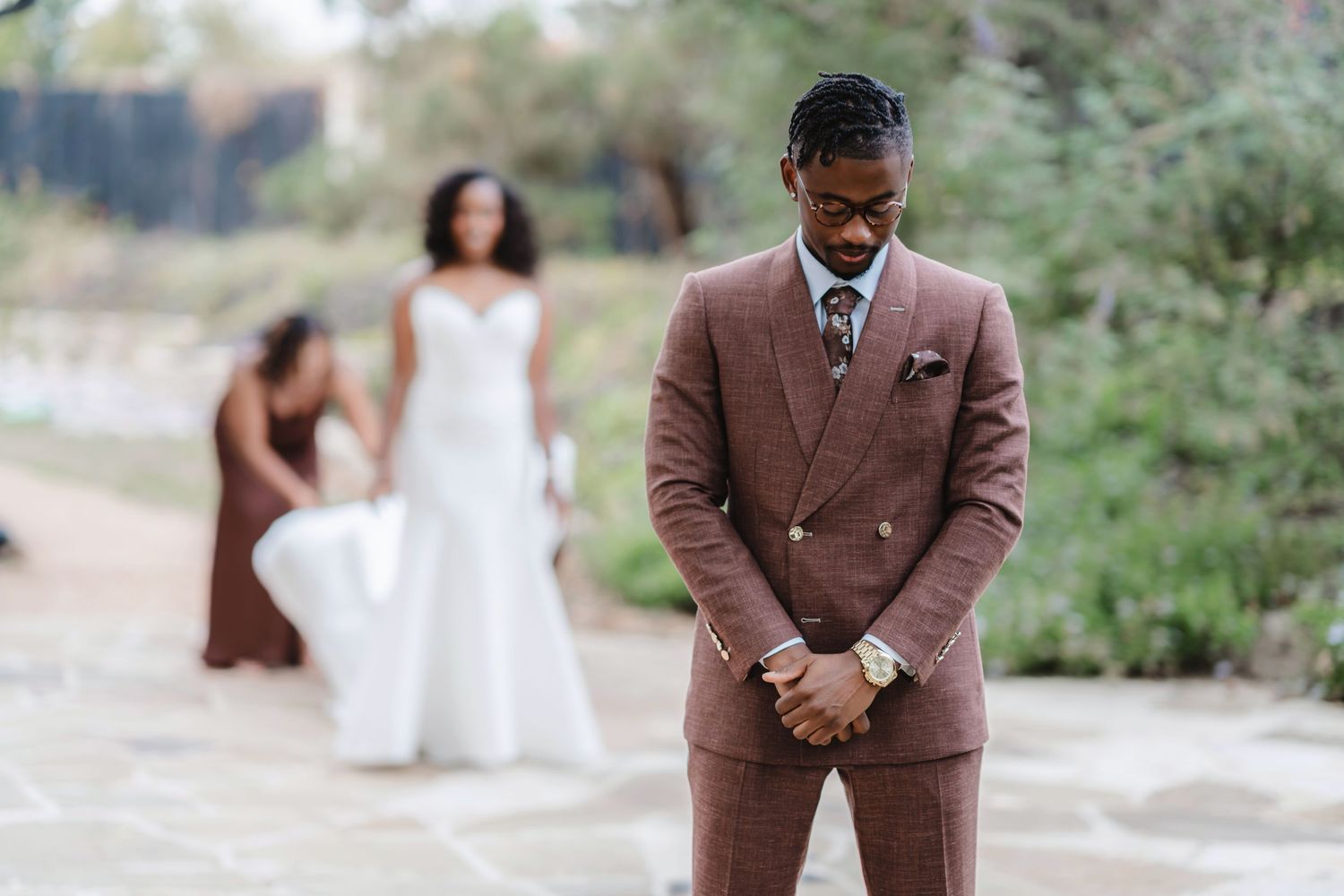 Elegant outdoor wedding portraits with a couple in brown suit and white gown against a natural backdrop.