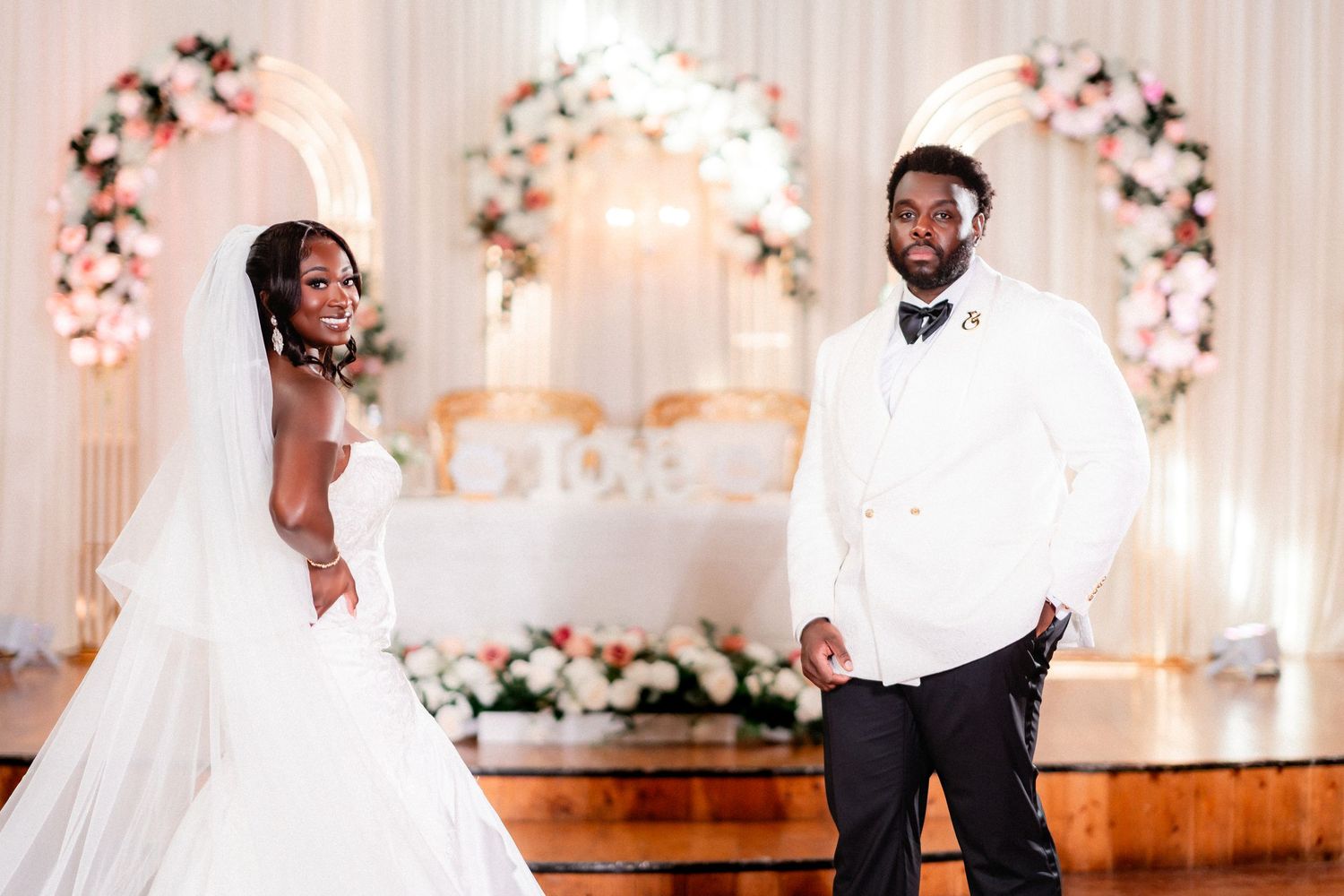A wedding celebration with floral decorations and elegant white drapery in an indoor venue.