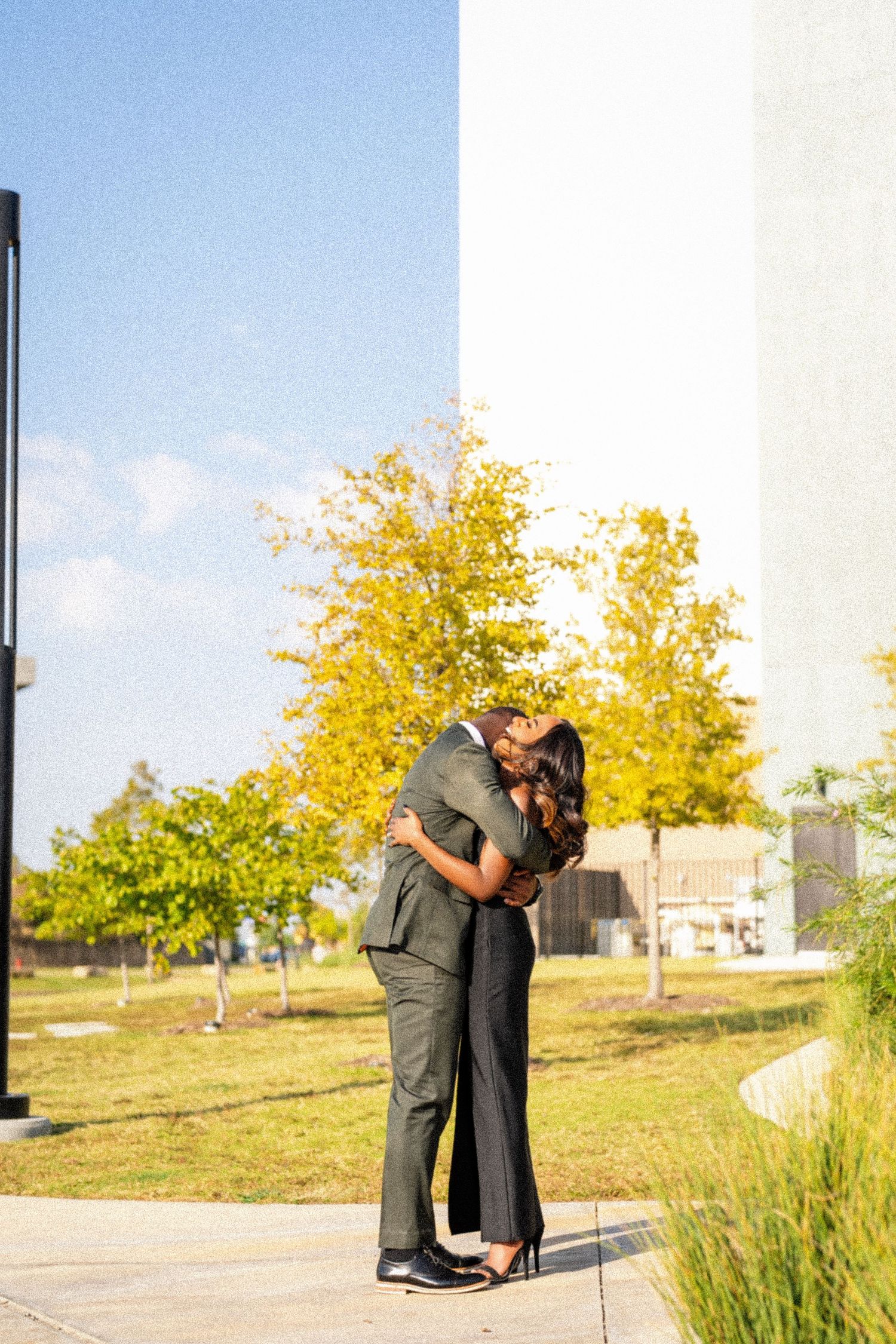 Couple sharing a romantic embrace outdoors with autumn trees in the background.