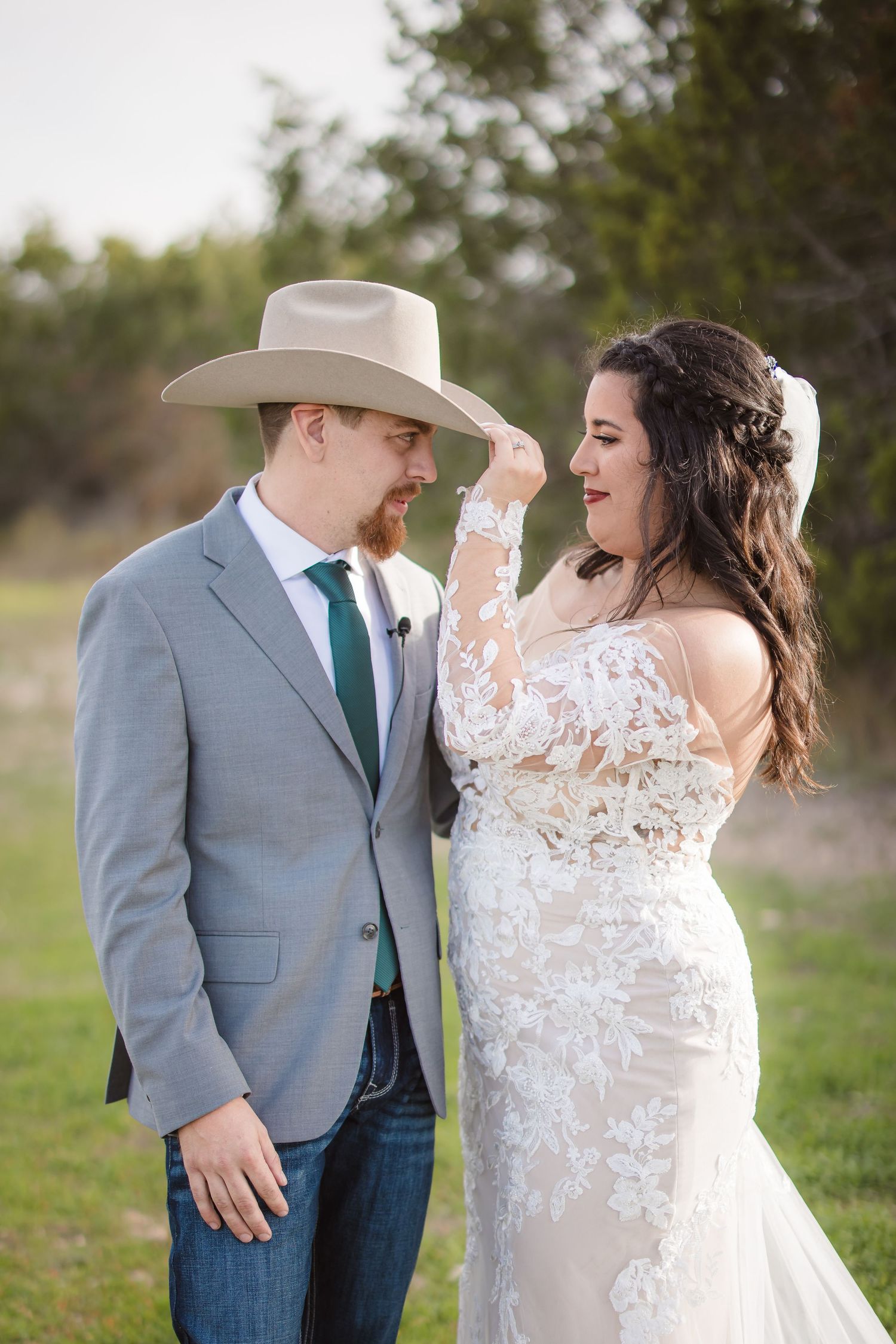 A romantic outdoor wedding moment captured with a couple in western attire including a cowboy hat and grey suit.