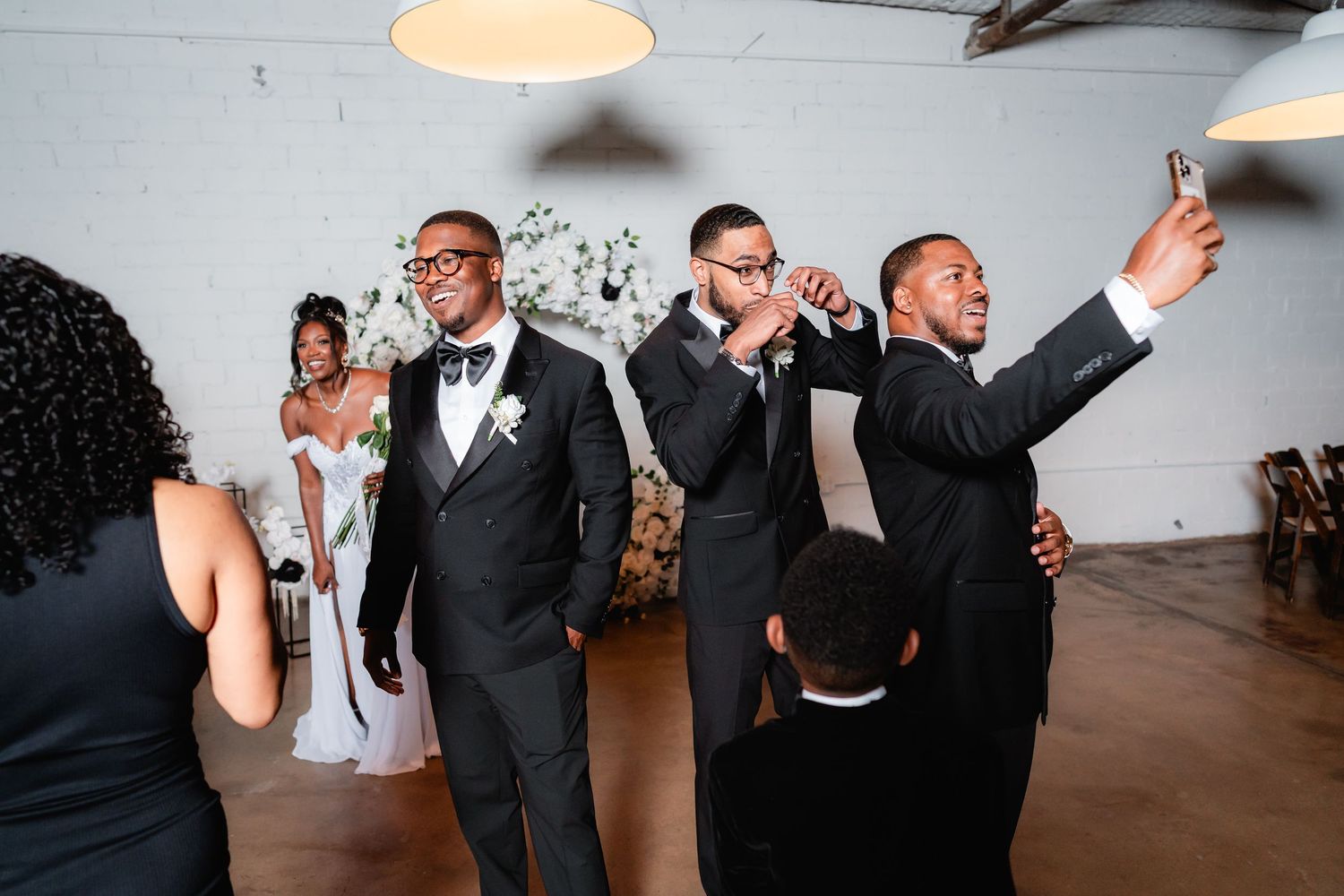 Wedding guests and party members celebrate on the dance floor at a modern indoor reception.