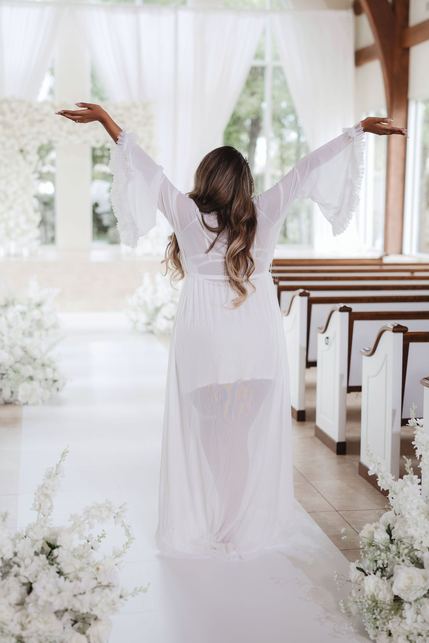 Figure in flowing white dress twirls in sunlit venue with white floral decorations.