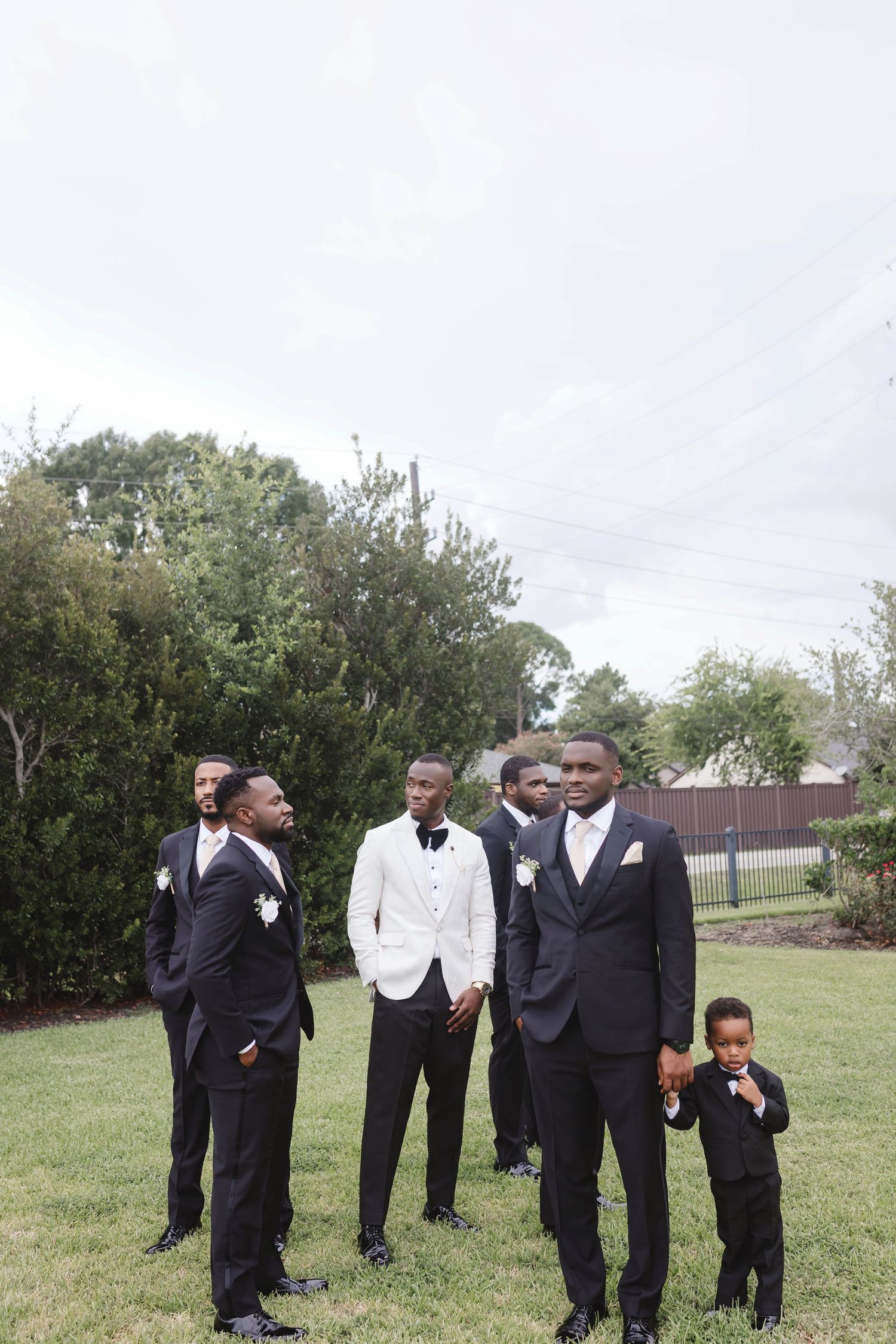 A group in formal attire gathers outdoors on a grassy lawn during a wedding celebration.
