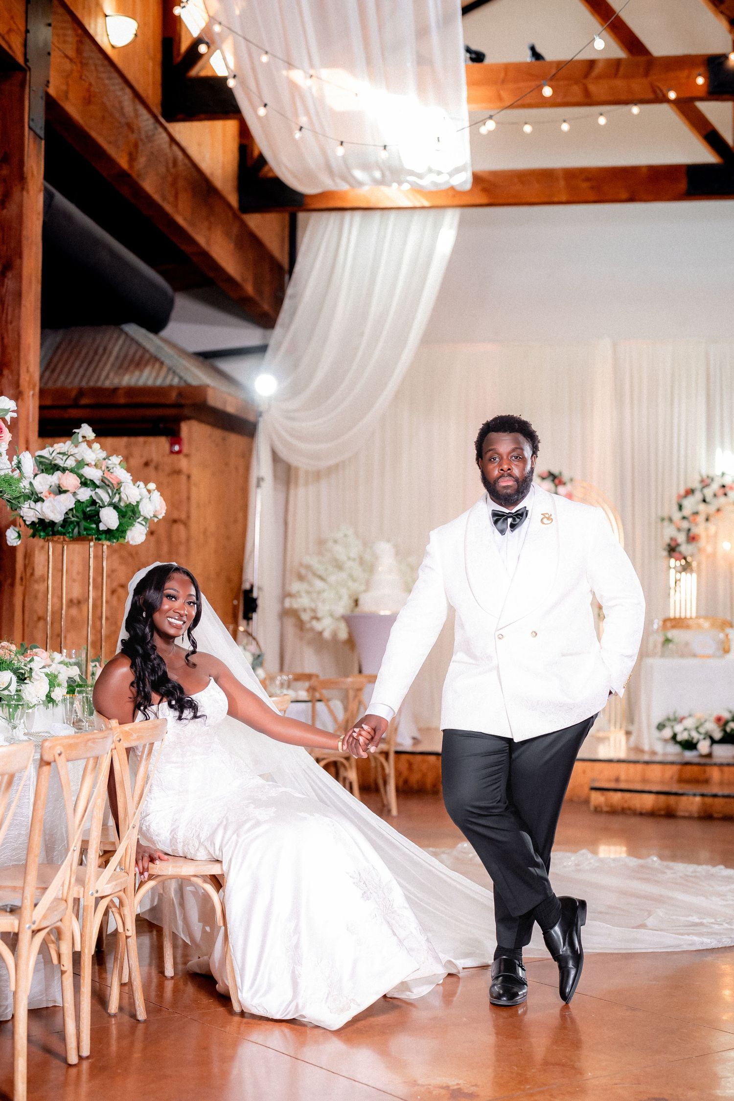 Newlyweds dance and twirl in a rustic barn venue decorated with white drapes and string lights.