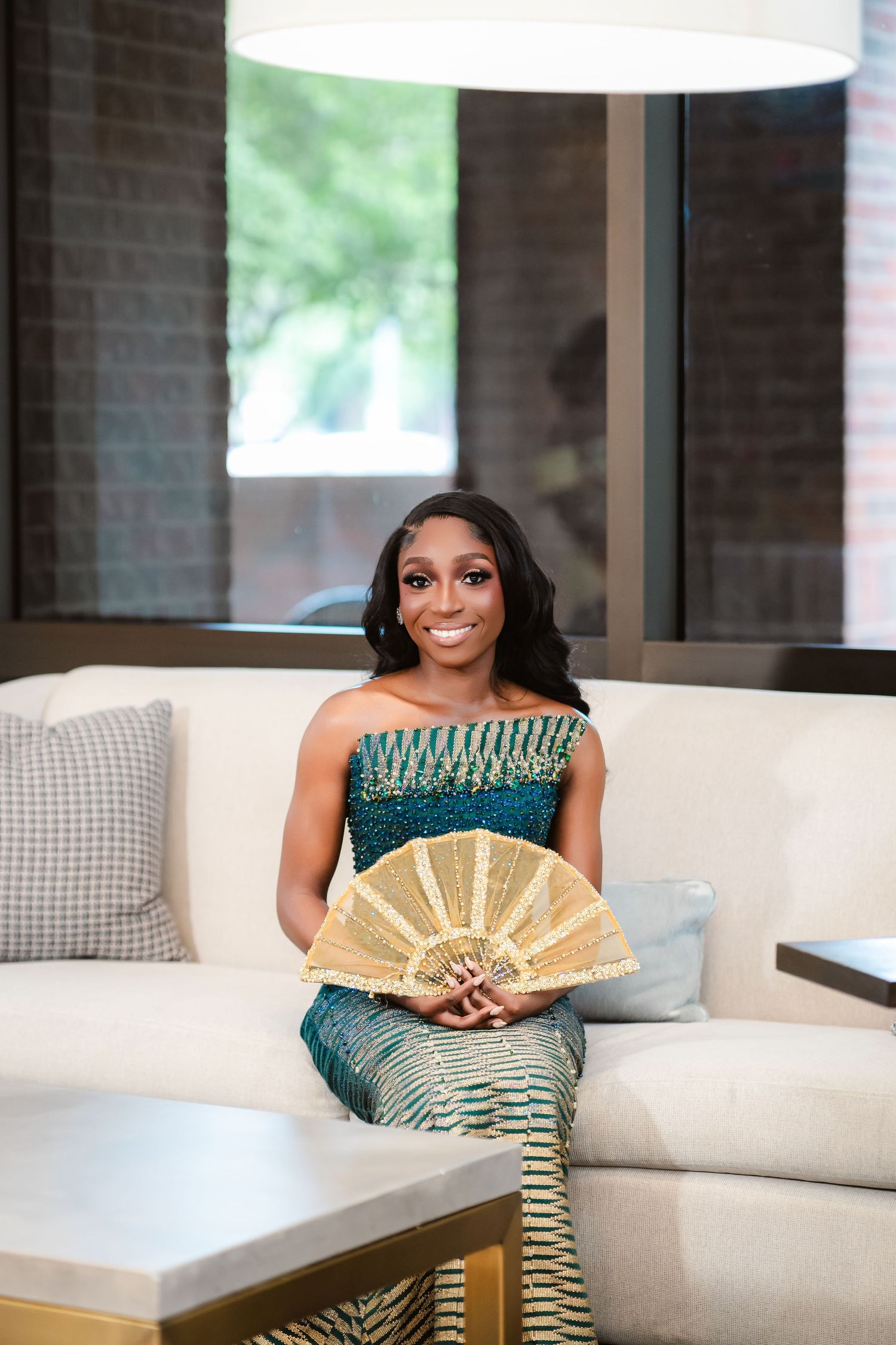 Elegant green dress and gold fan on a white couch in a modern interior setting.