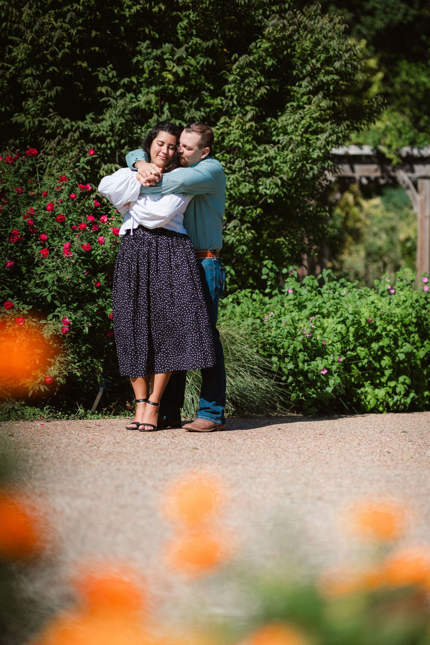 A tender embrace shared between a couple in a garden with orange poppies and red roses in bloom.