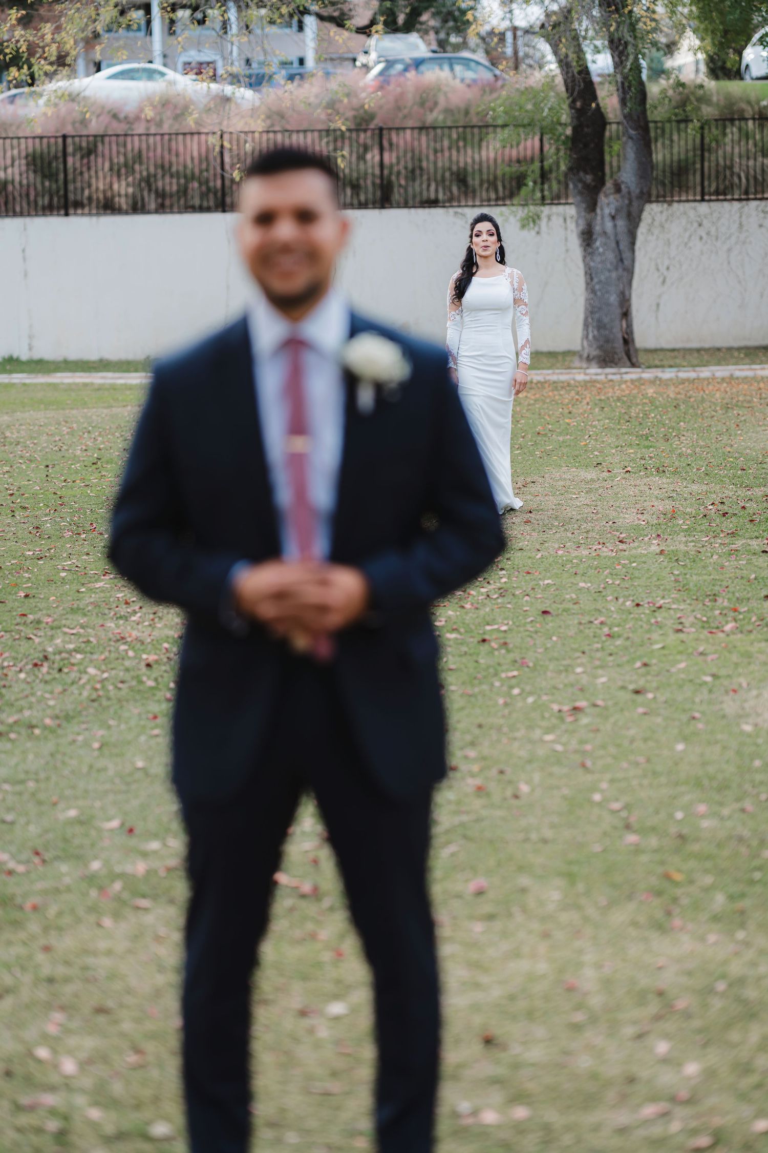 Outdoor wedding scene on a grassy lawn with trees and autumn foliage in the background.