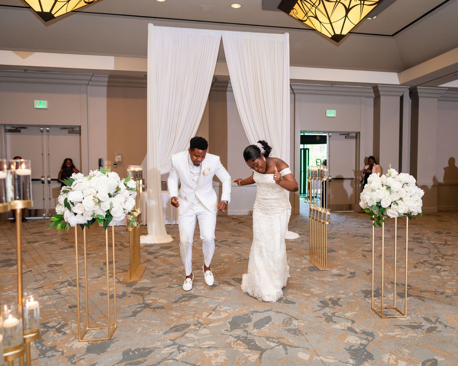 Wedding venue staff setting up decorative white fabric drapes and gold pedestals in a ballroom.