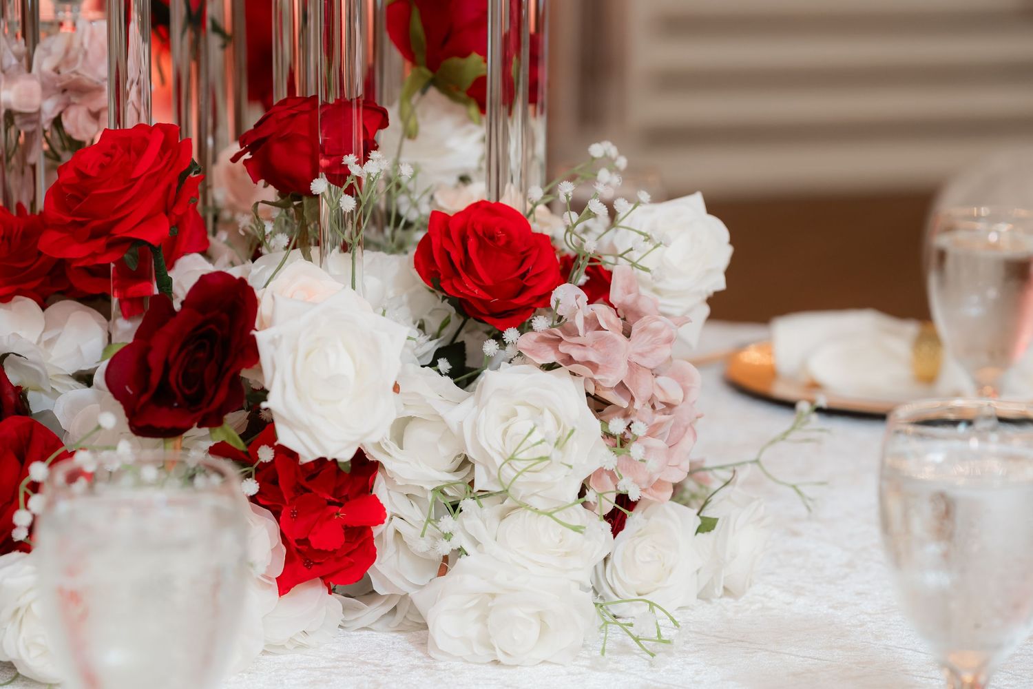 Elegant wedding reception table decorated with red and white roses in crystal vases and glassware.