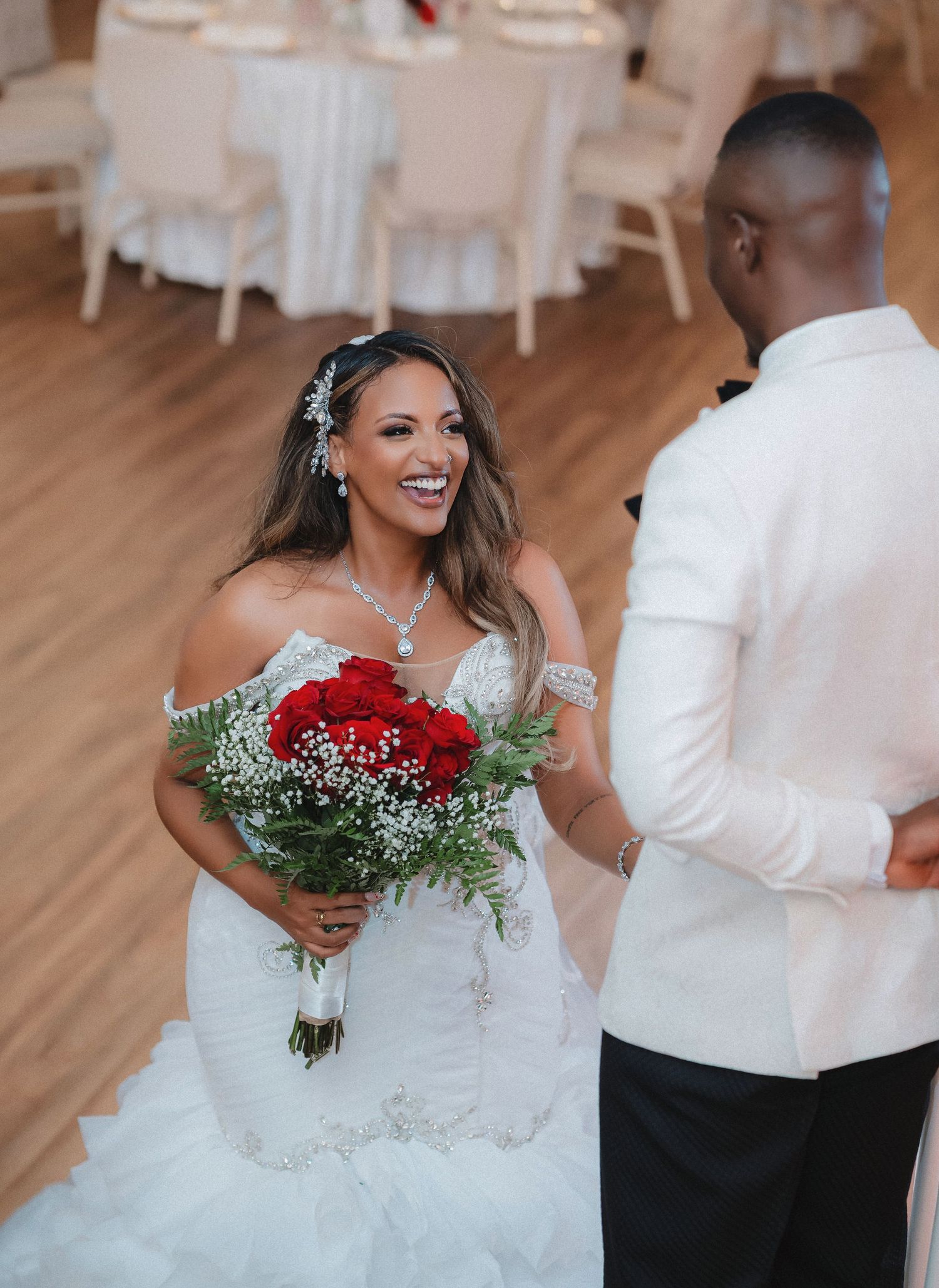 A bride in a white gown holds a vibrant red rose bouquet while dancing at her wedding reception.