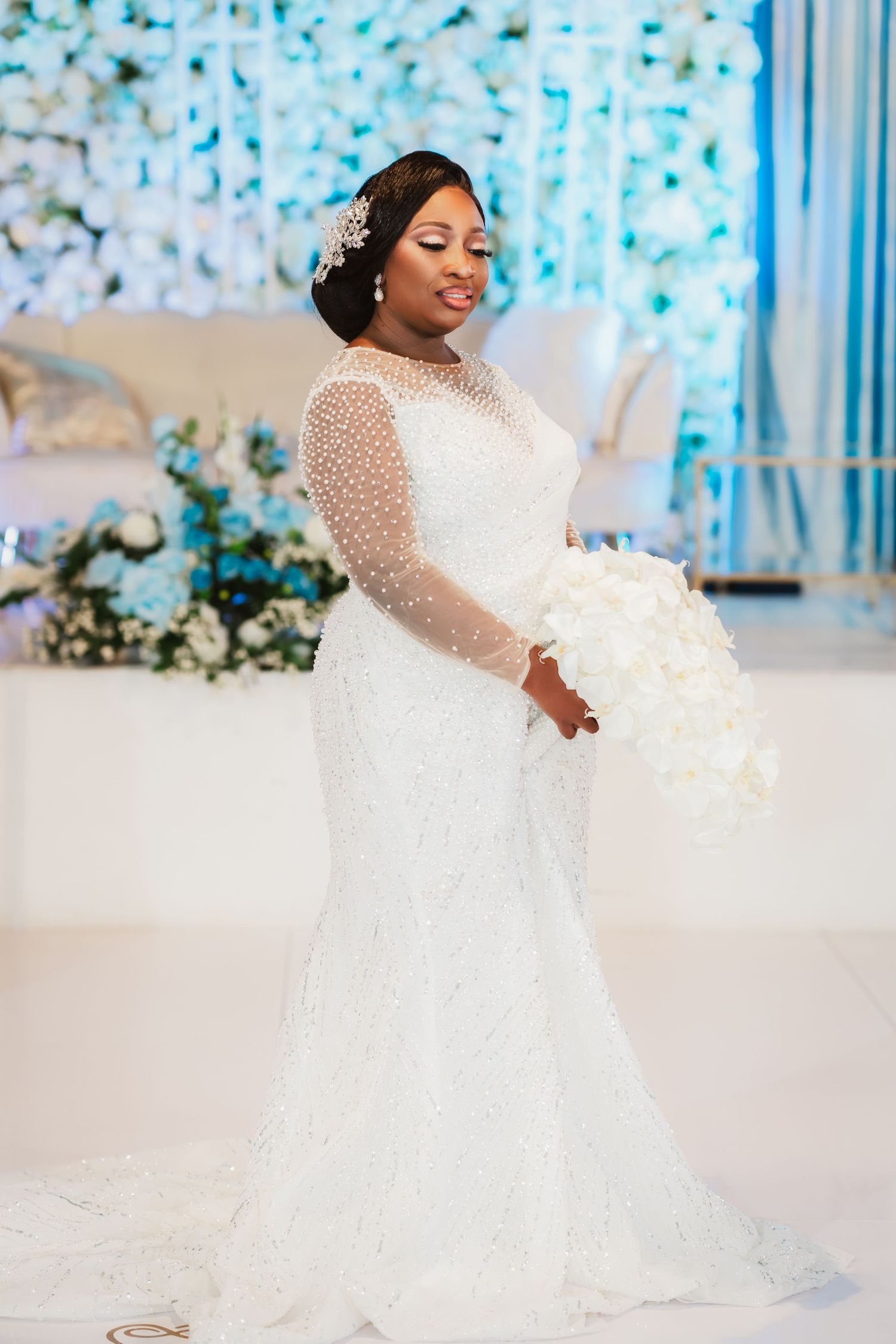 An elegant white beaded wedding dress with long sleeves and full skirt in a bright blue-lit venue.