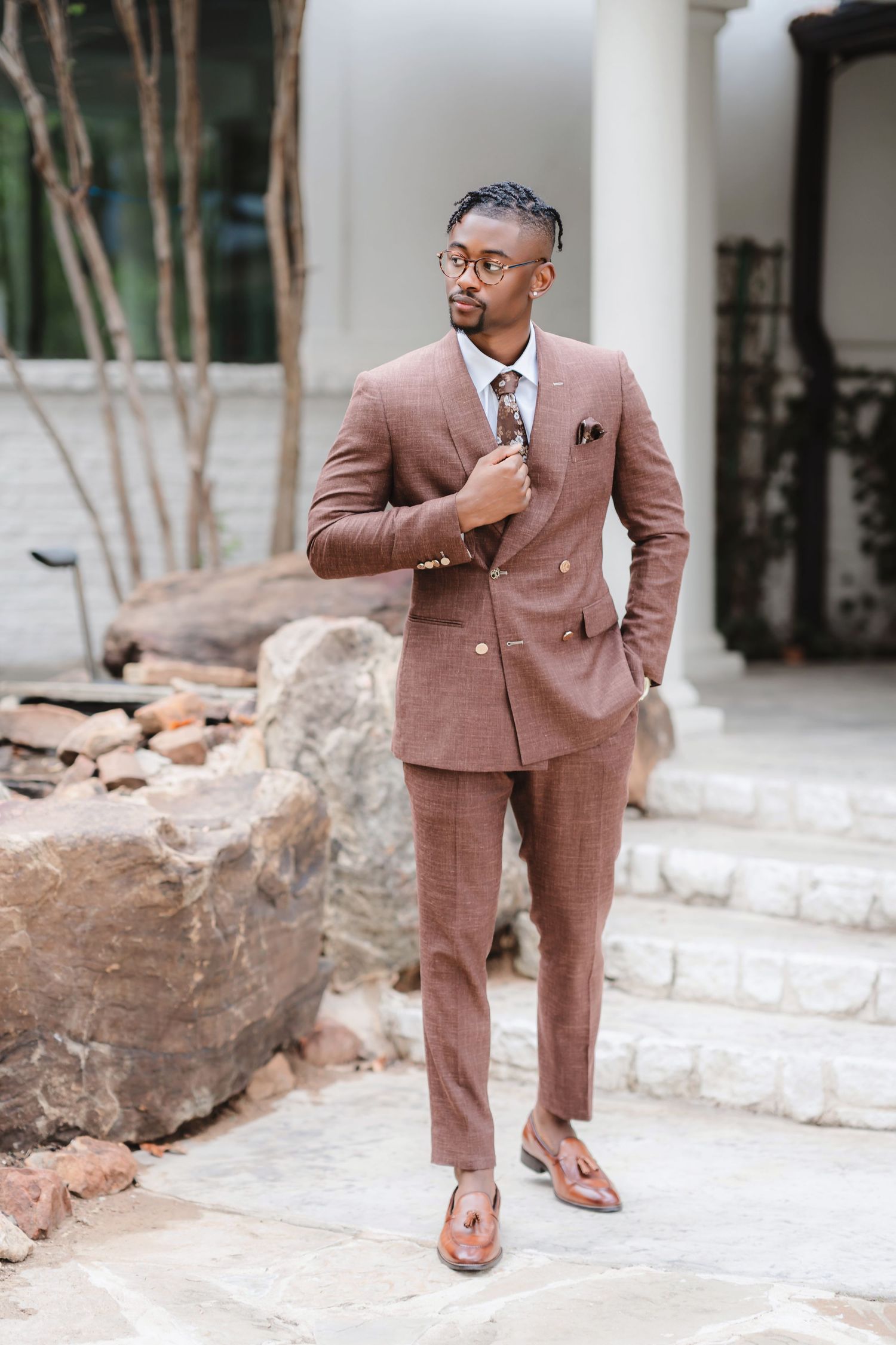 A stylish brown suit is showcased in multiple poses against a stone wall backdrop.