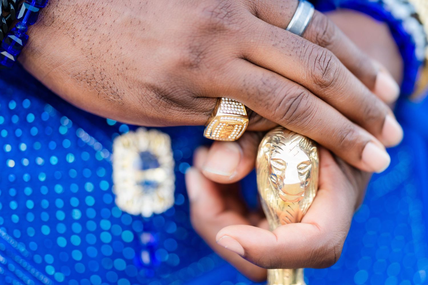 Close-up of hands wearing ornate gold rings against a bright blue background.