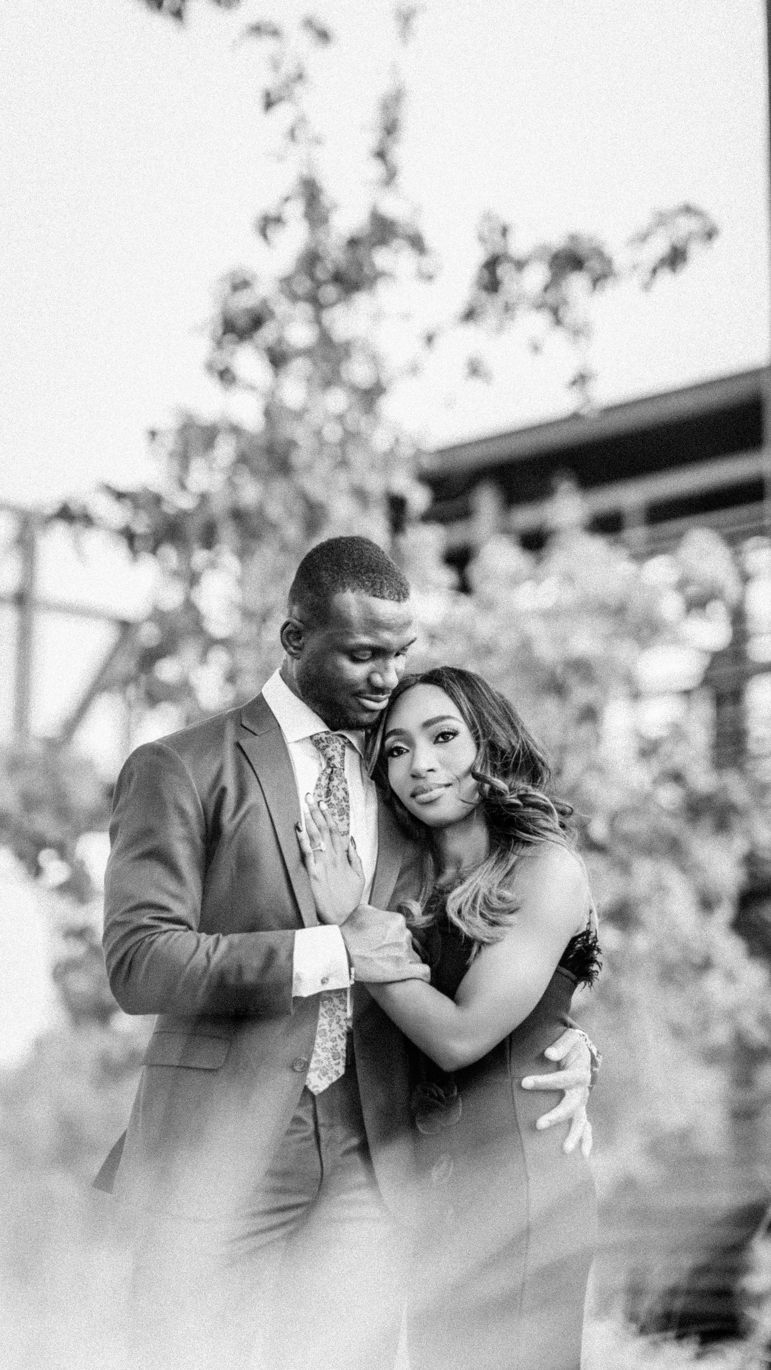 A soft focus black and white portrait of a couple embracing outdoors among trees.