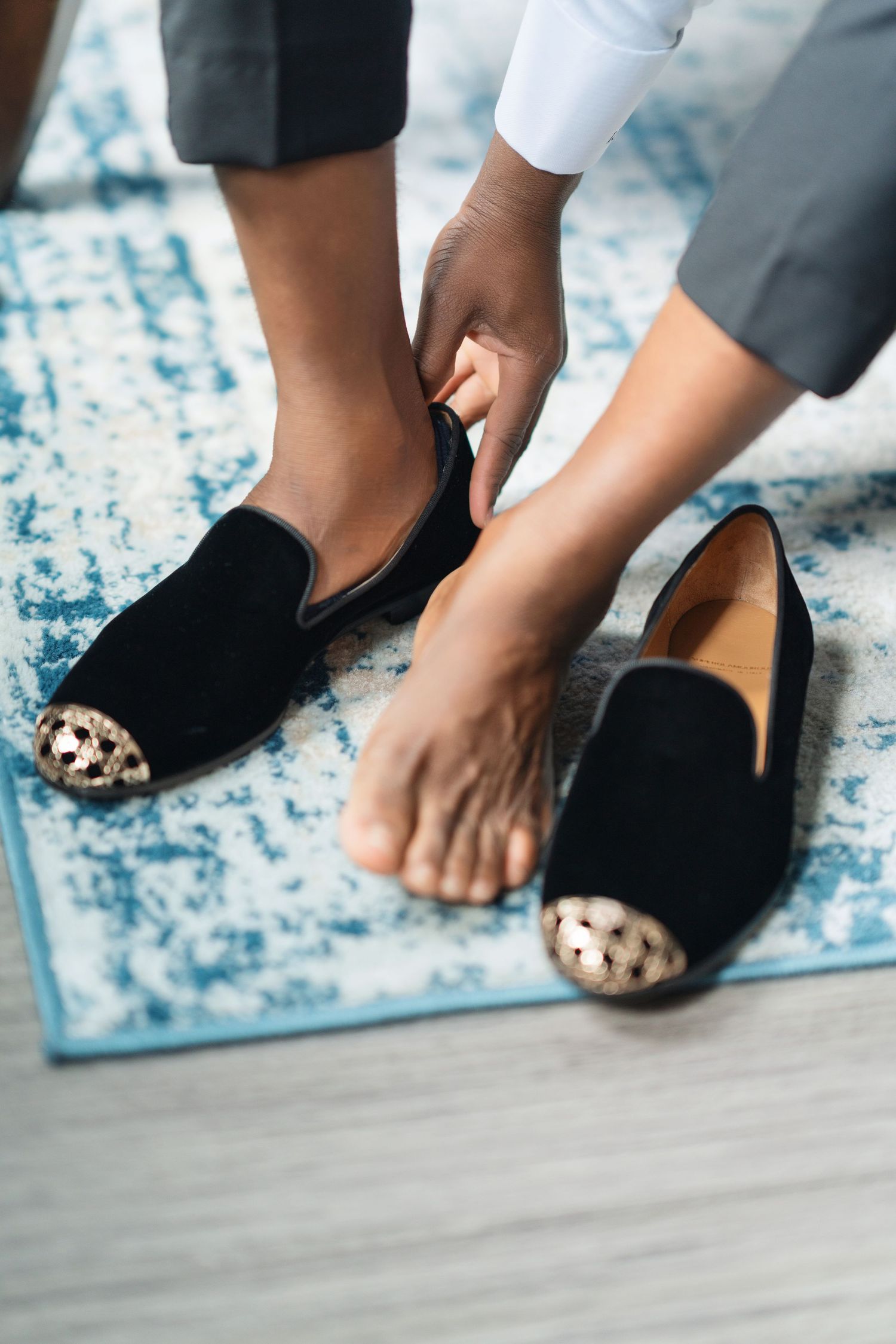 Black formal loafers with decorative details shown on a blue and white patterned rug.