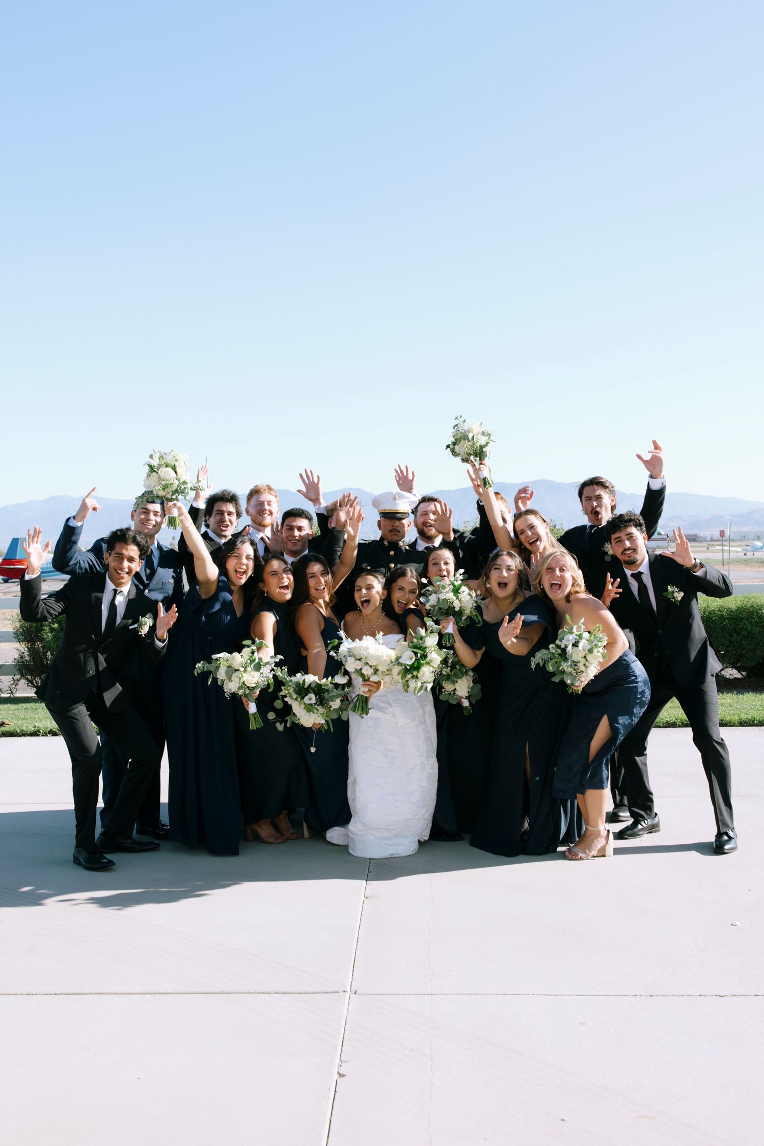 Joyful wedding party members raise their arms in celebration during a group photo.