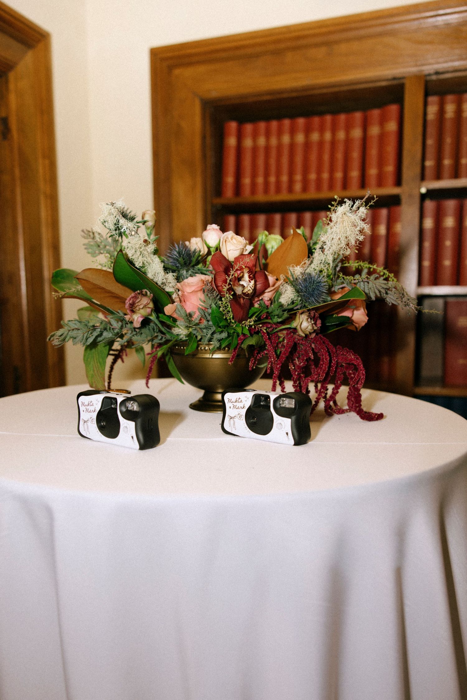 White tablecloth with floral centerpieces against a backdrop of wooden bookshelves.