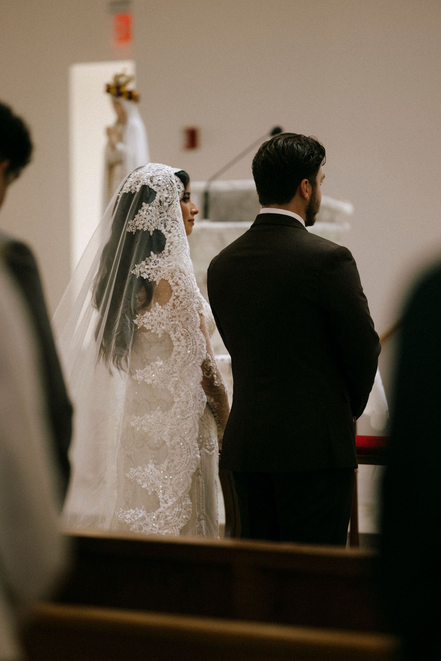 Side view of a couple during their wedding ceremony in a church with wooden pews.