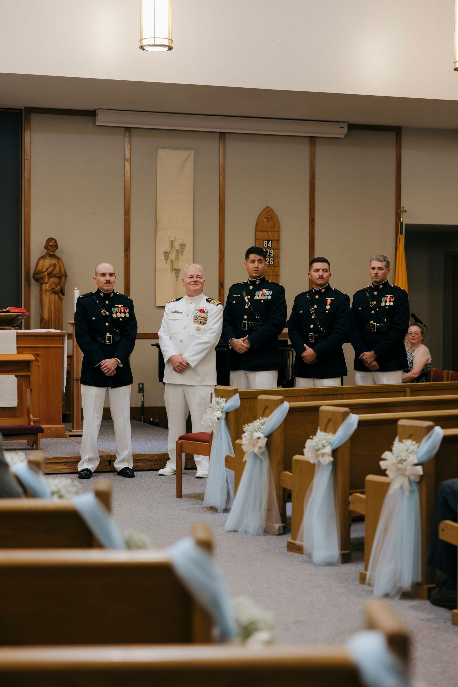 Military groomsmen in dress uniforms standing at church altar during wedding ceremony with decorated pews.