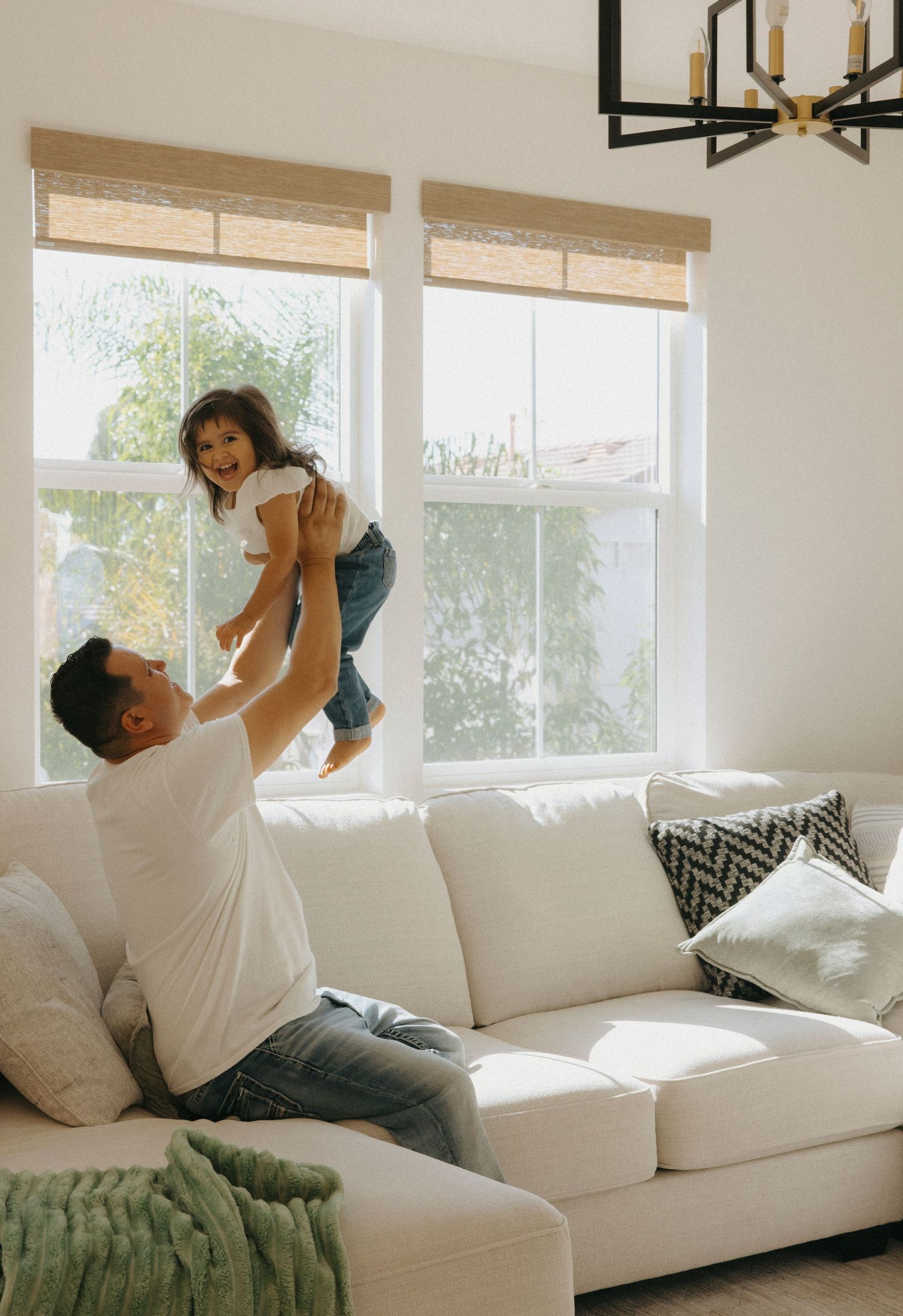 Playful family moments captured on a white sectional sofa in natural lighting.