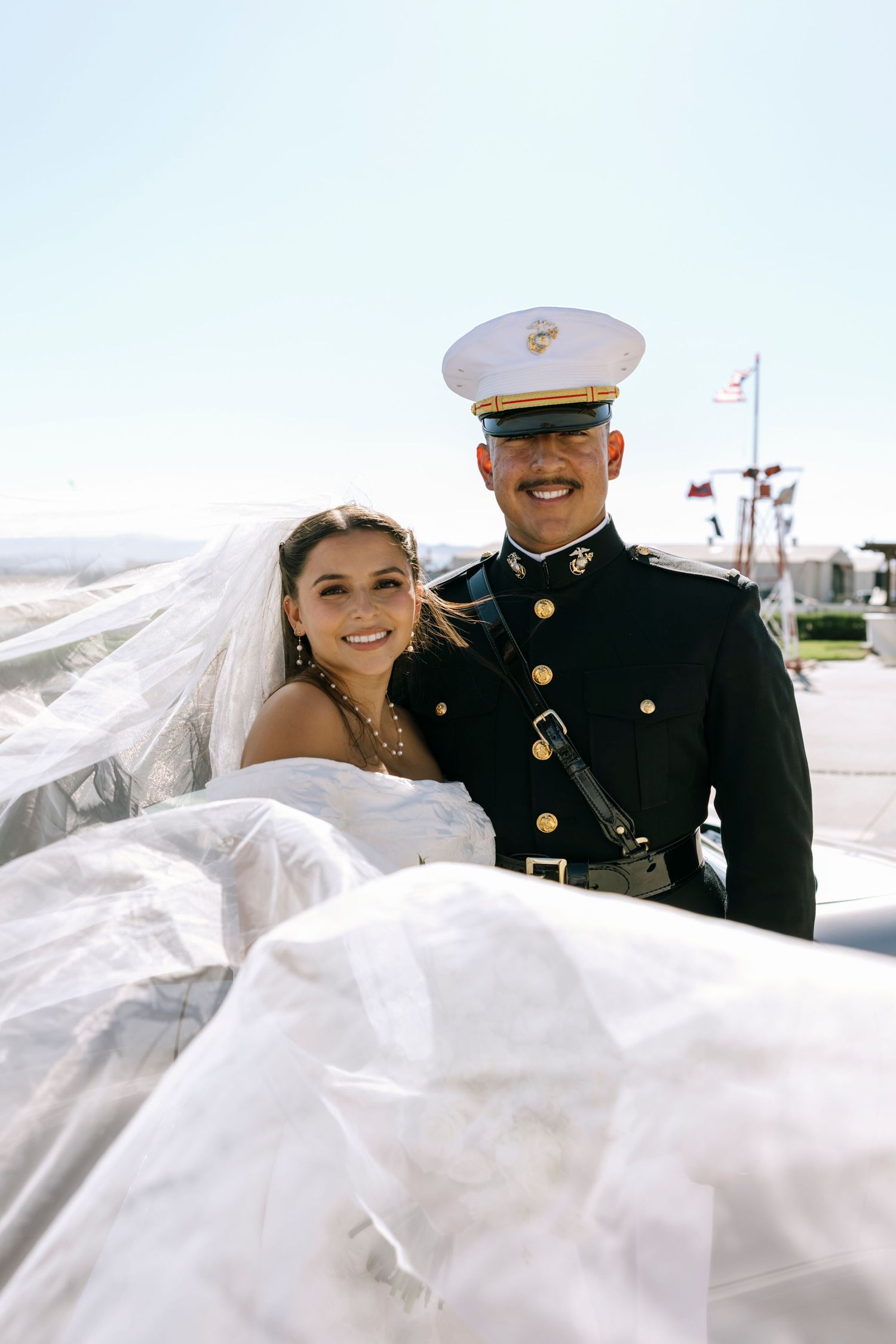 A flowing veil catches the breeze during outdoor military wedding portraits.